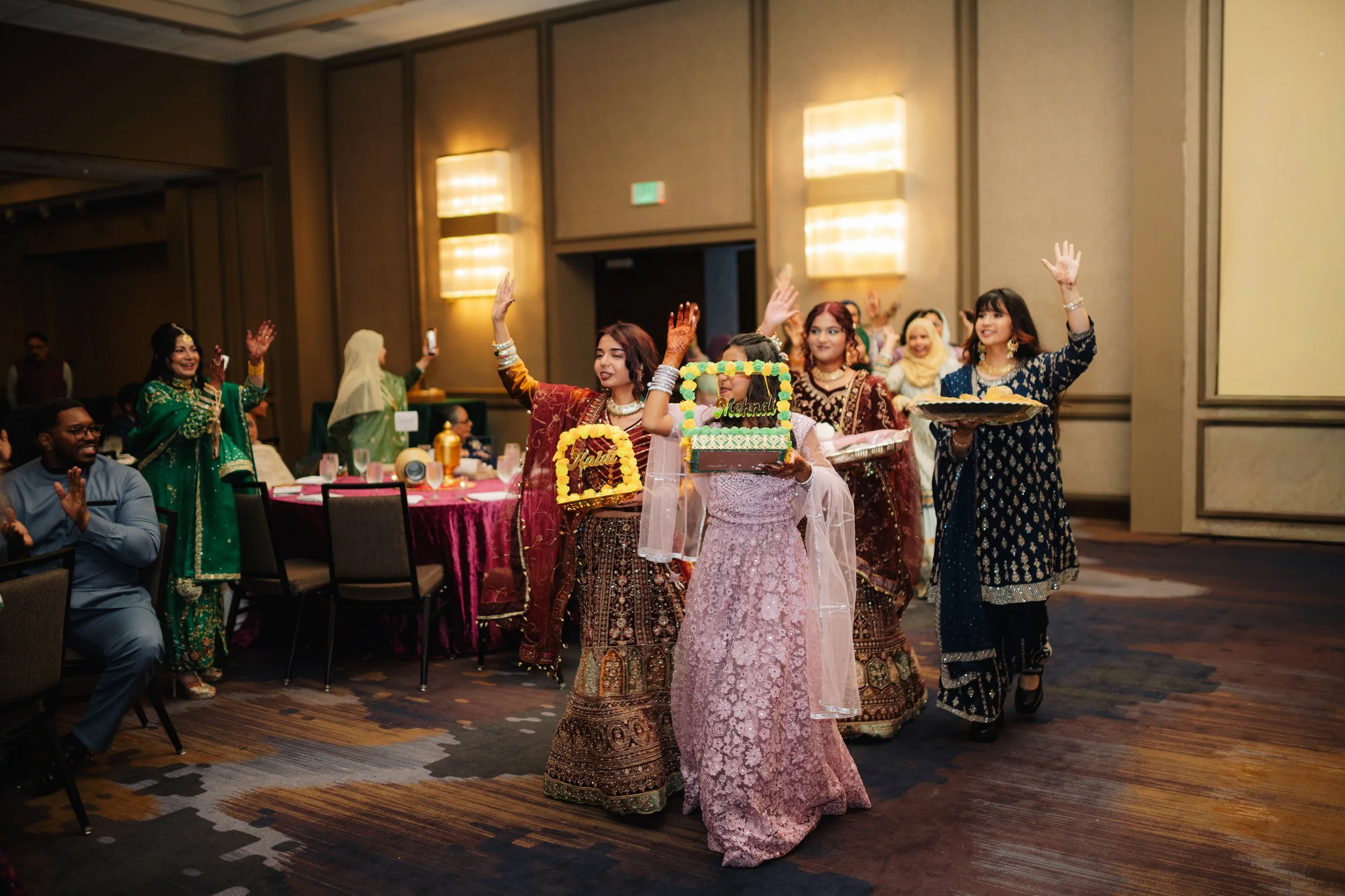 Group of women and children in traditional Indian attire celebrating at a banquet hall with festive decorations.