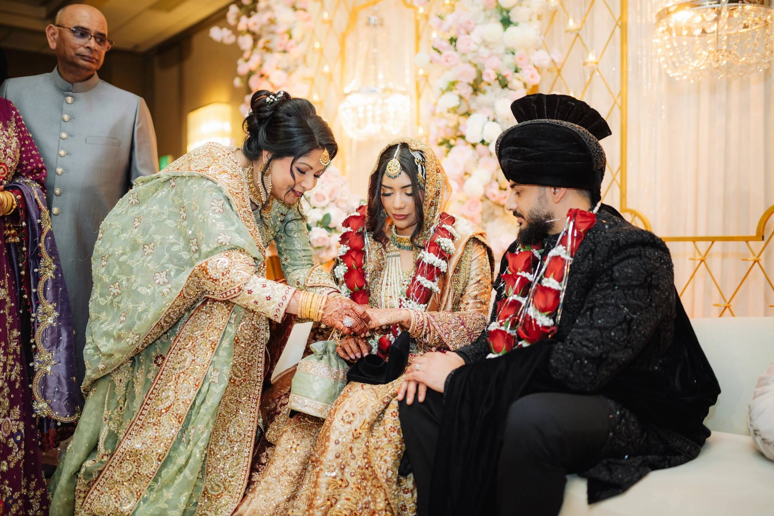 Indian bride and groom during wedding ceremony, with family members present, in decorated venue with flowers and lights.