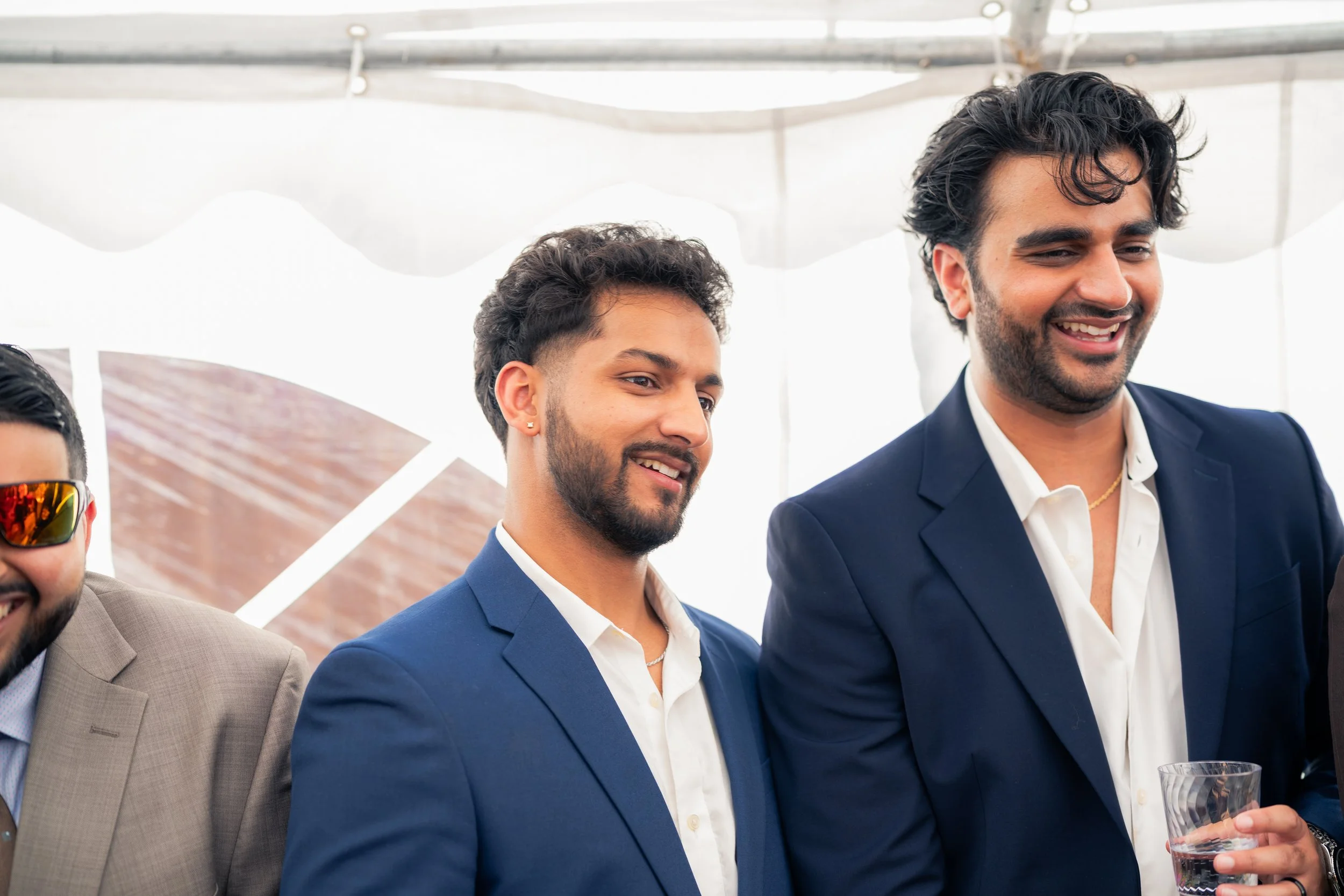 Group of men dressed in suits at a social event, smiling and holding a glass of water.