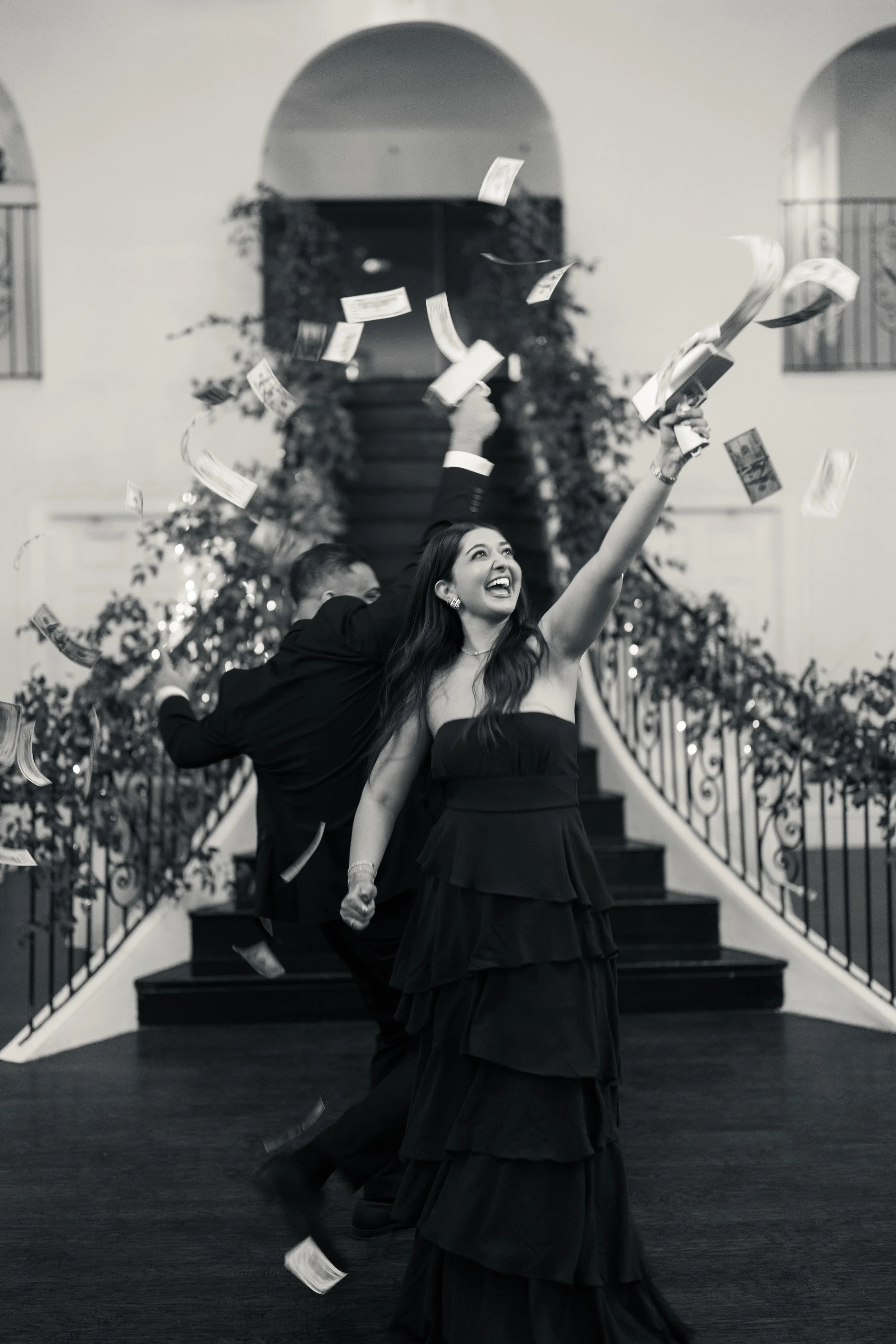 A woman in a black dress joyfully celebrating as money falls around her indoors.