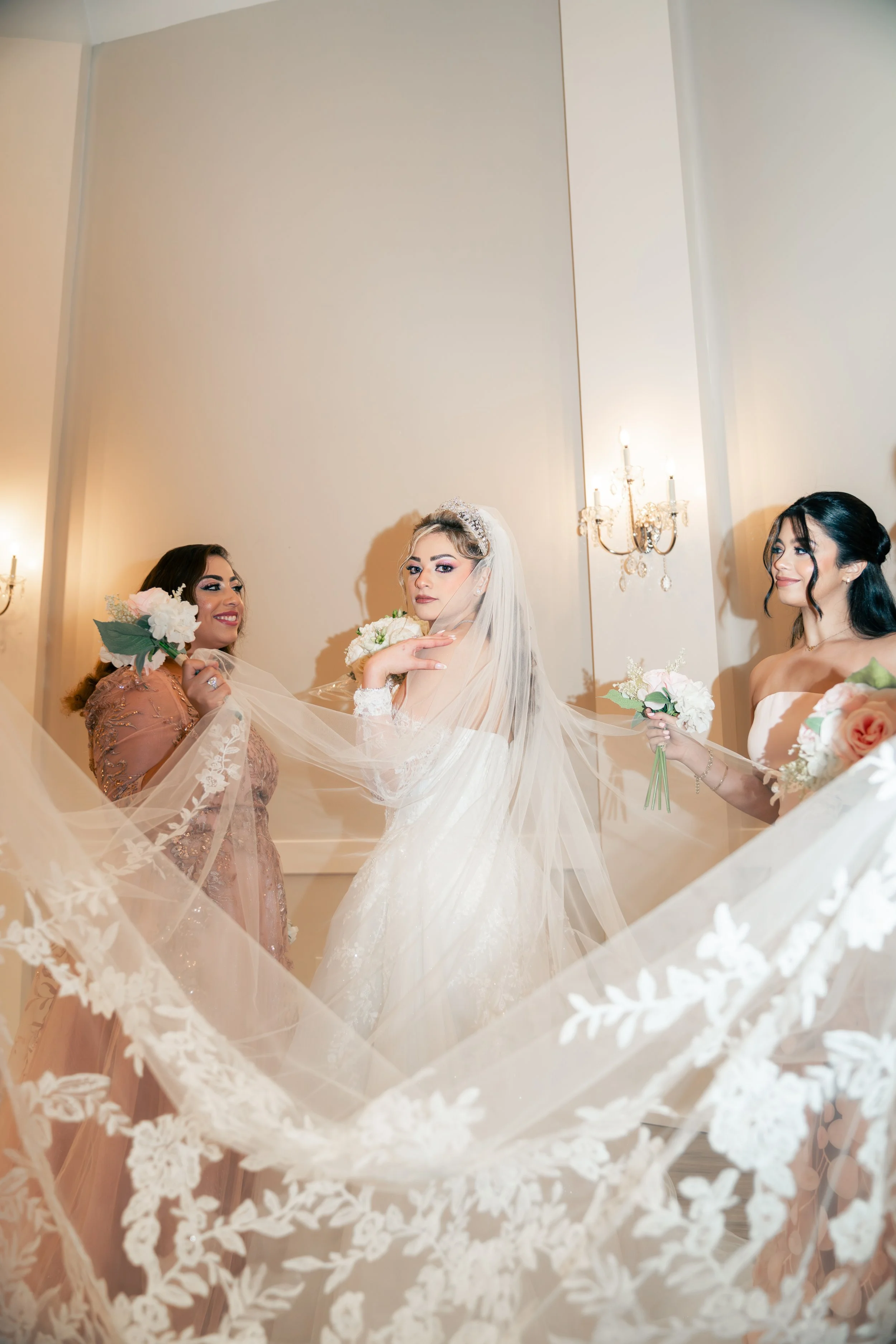 A bride in a wedding dress with a veil surrounded by her bridesmaids holding bouquets.