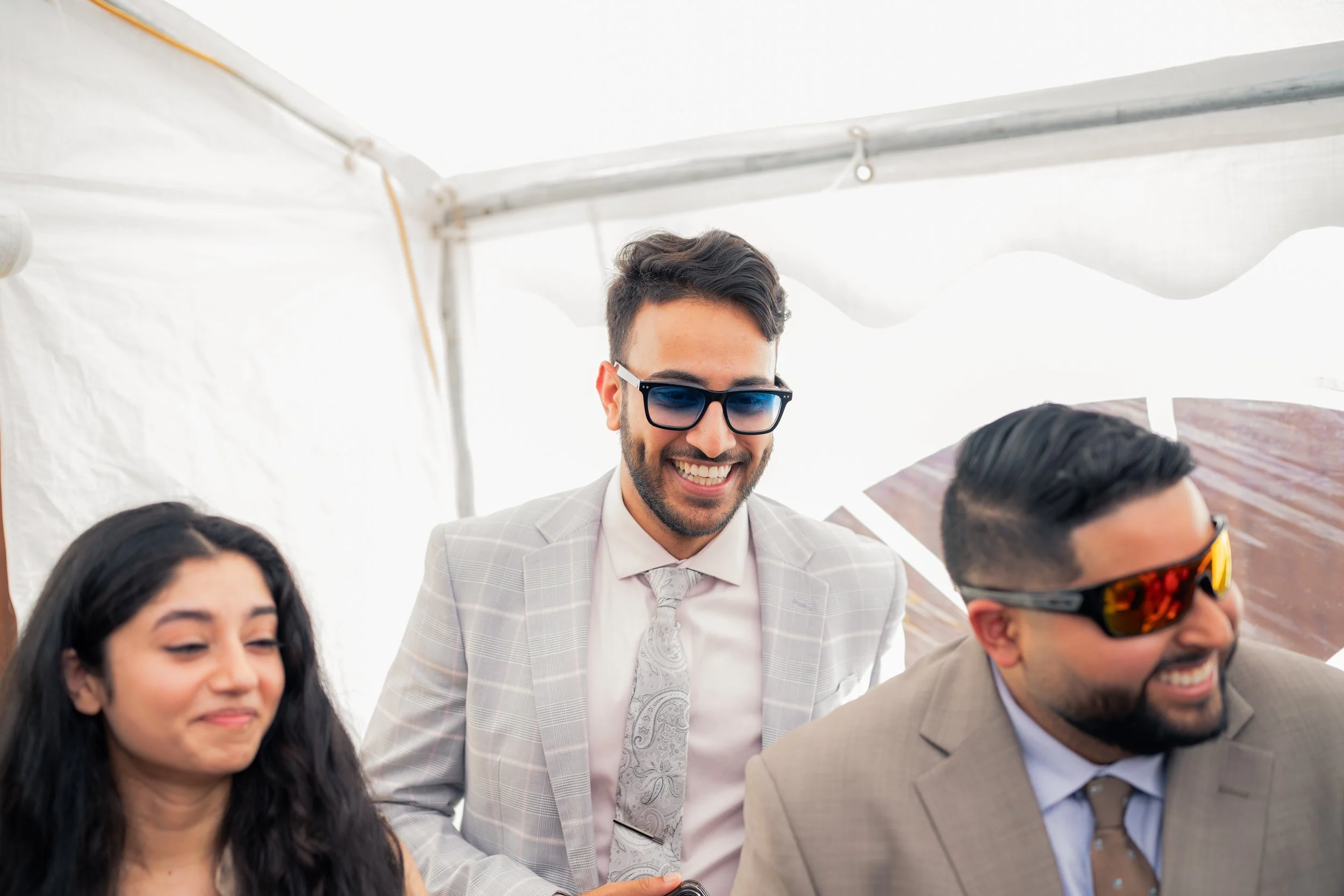 Three people in suits and sunglasses at an outdoor event, smiling and enjoying themselves.