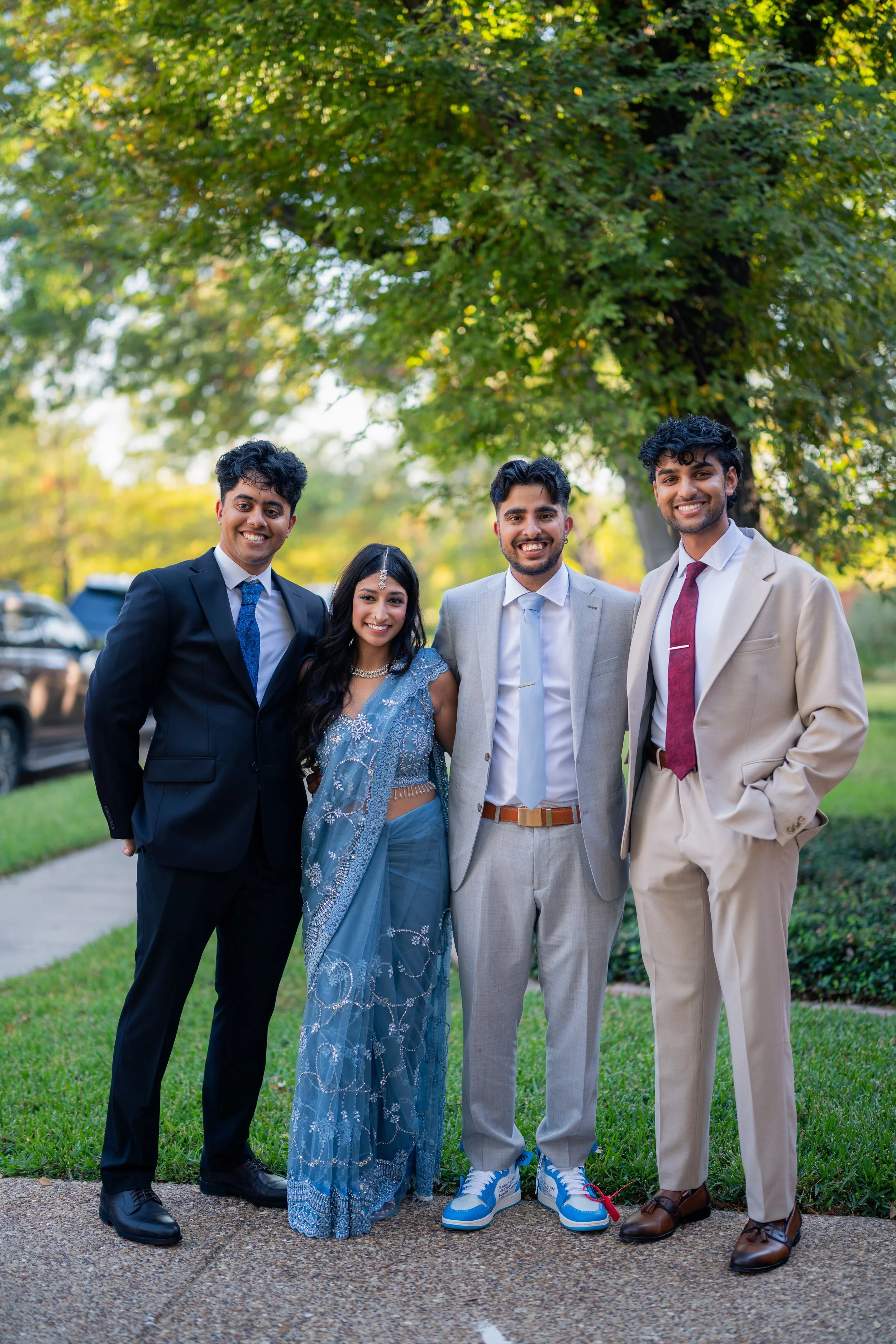 Group of four people standing outdoors in a park, dressed in formal attire, smiling at the camera.