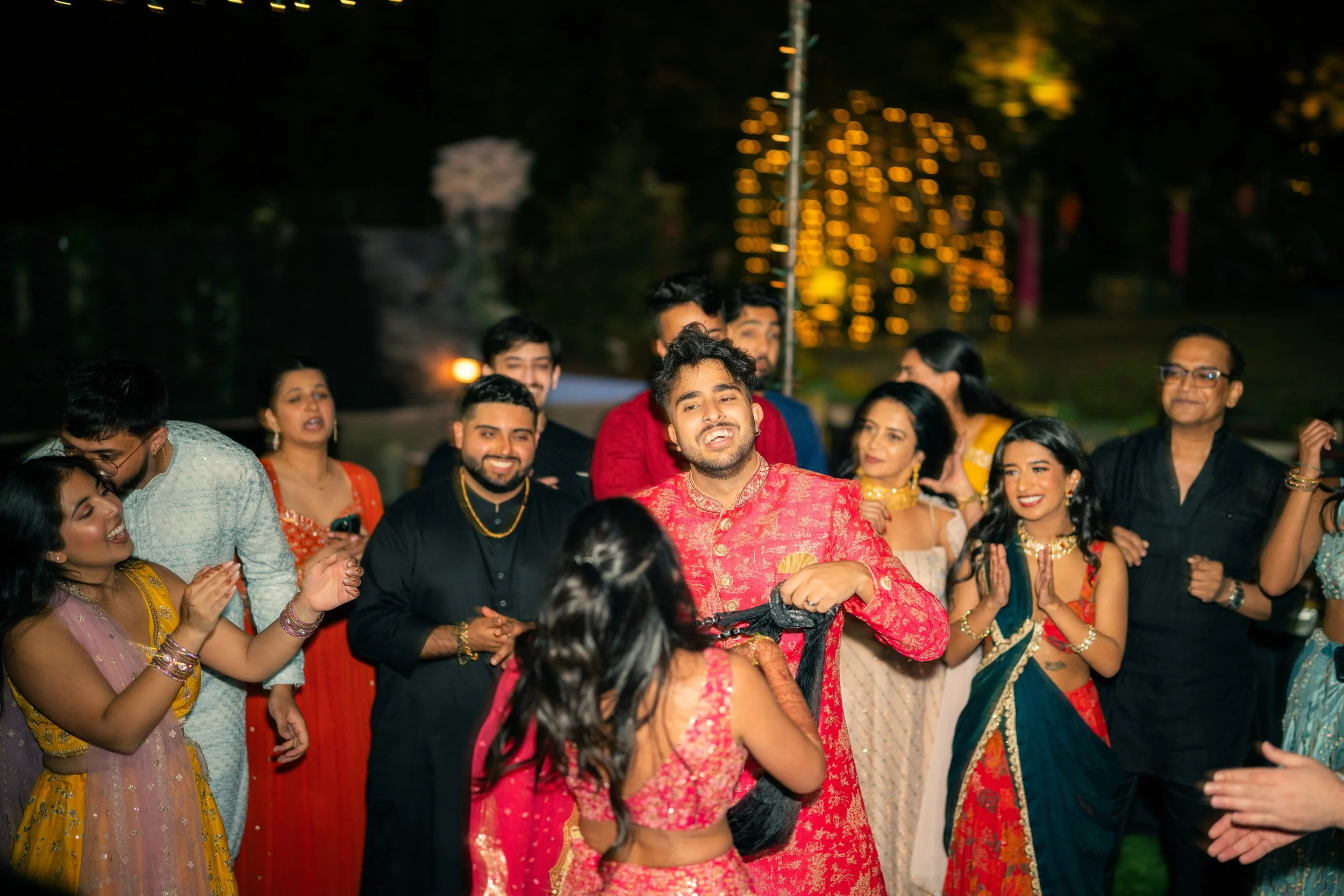 A group of people dressed in colorful traditional Indian attire celebrating at an outdoor wedding reception, dancing and enjoying the evening.