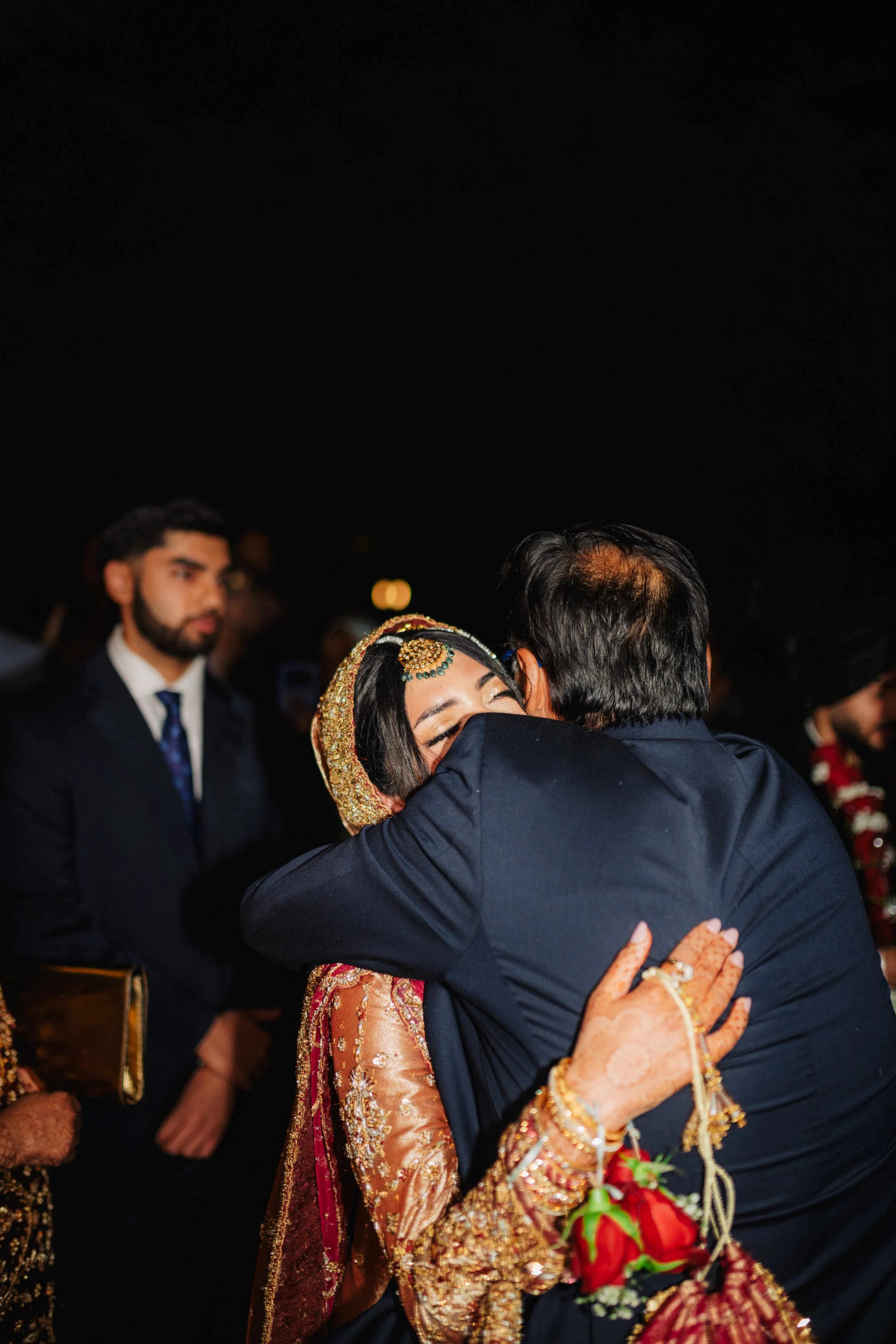 A woman in traditional Indian attire and jewelry is hugging a man at a celebration or wedding.