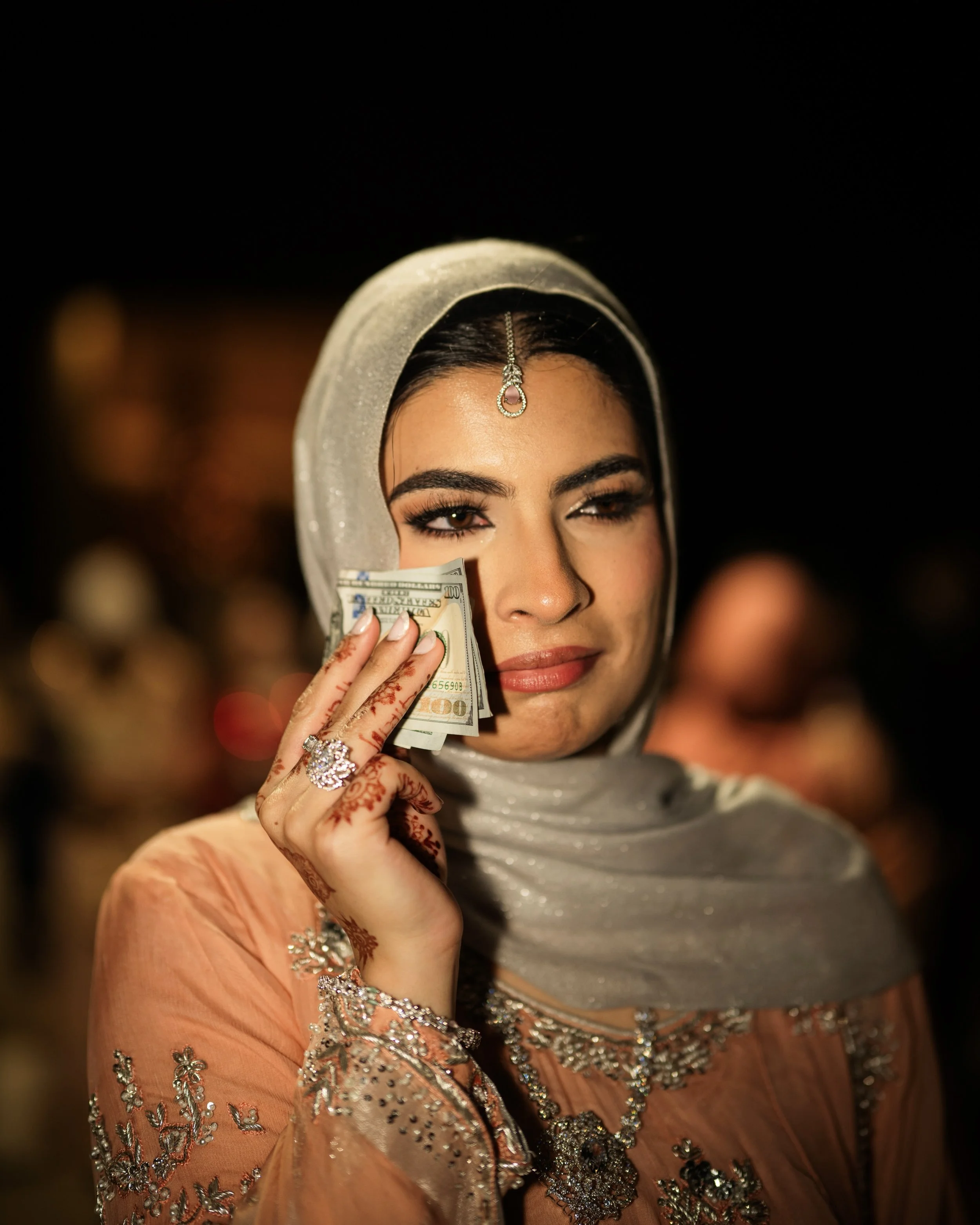 Woman in traditional attire holding dollar bills to her face, outdoors at night.