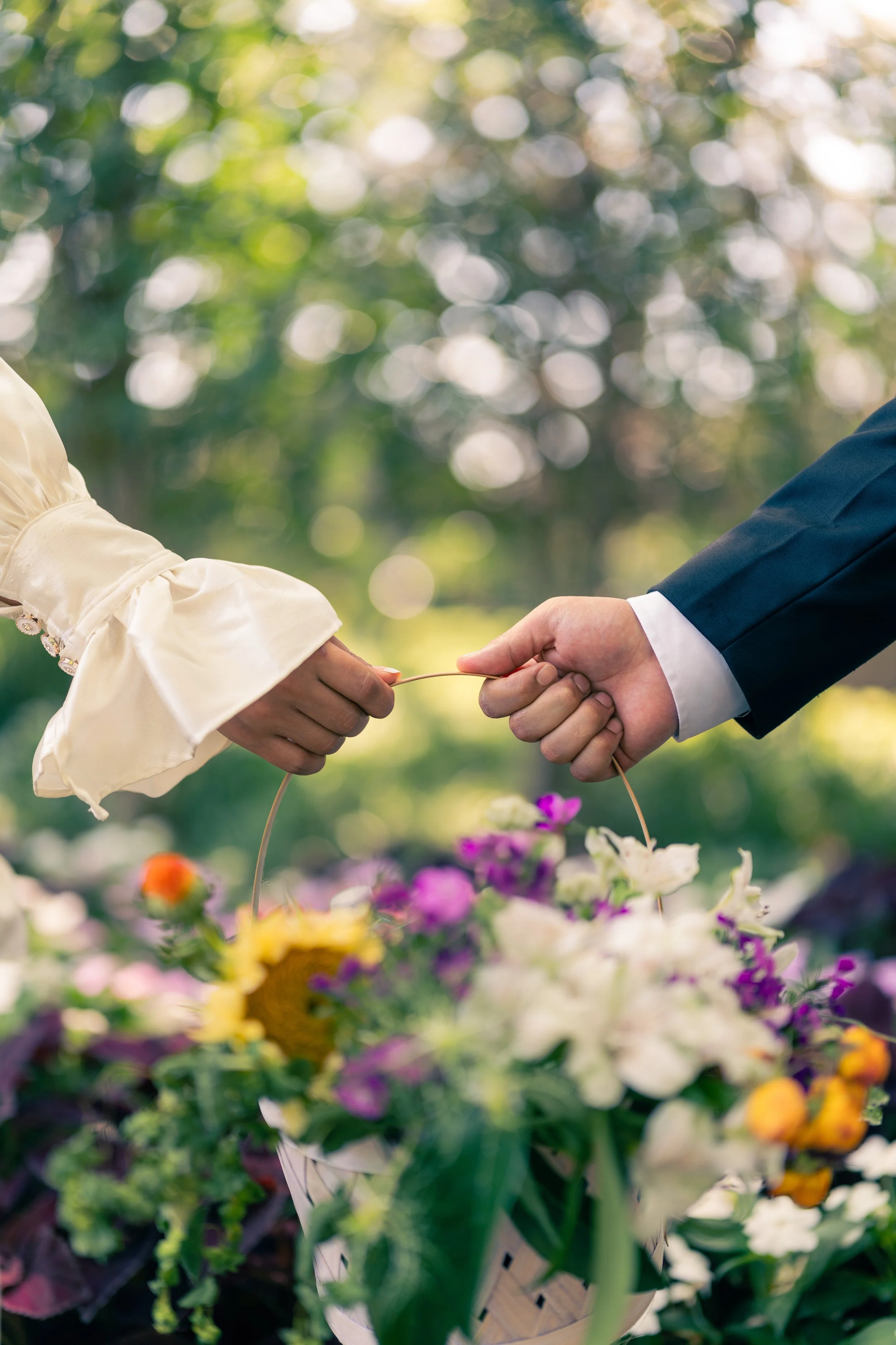 Two people exchanging wedding rings during a wedding ceremony outdoors, with flowers and greenery in the background.