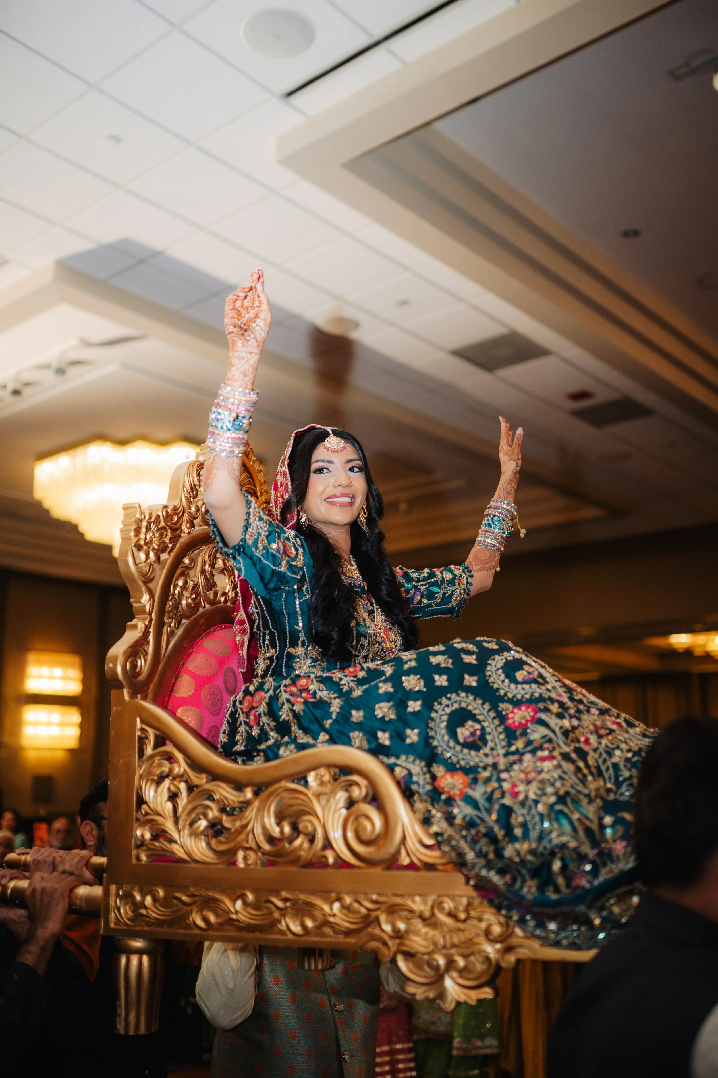 A woman dressed in traditional Indian attire riding on a decorative palanquin or palki, surrounded by people in a festive or ceremonial setting.