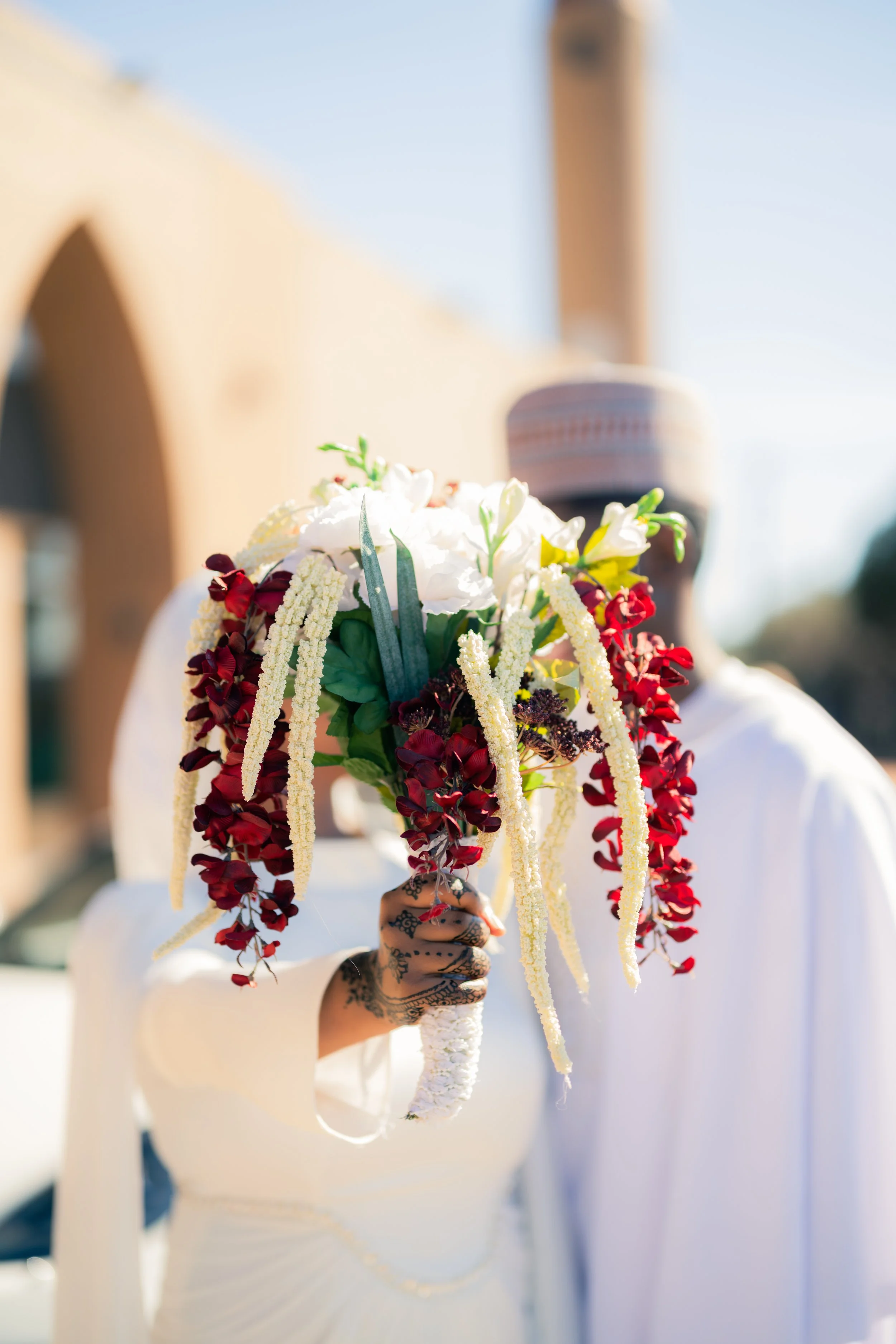 Person holding a colorful bouquet of flowers in front of their face, wearing a white dress with long sleeves.