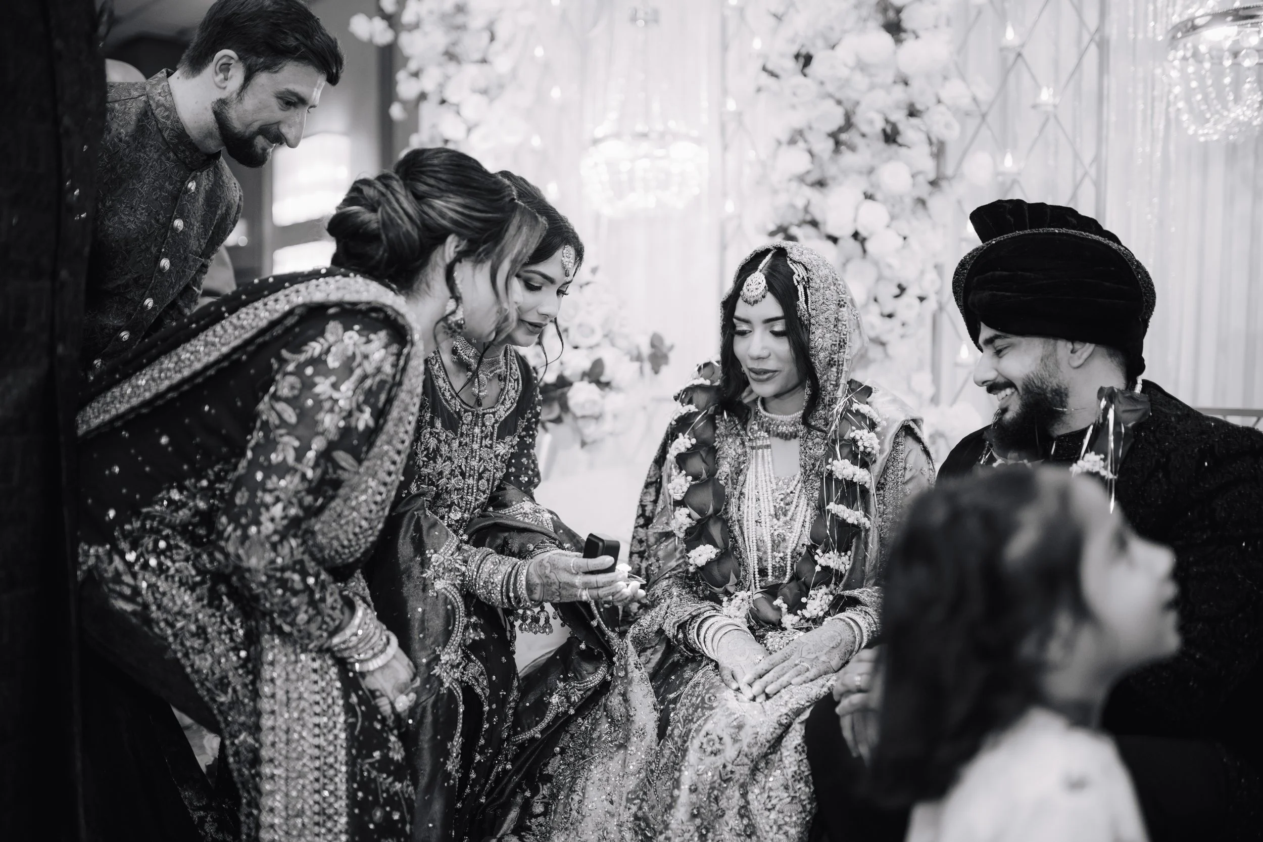 A group of South Asian bride and groom and family members at a wedding, dressed in traditional Indian attire, sharing a moment together.
