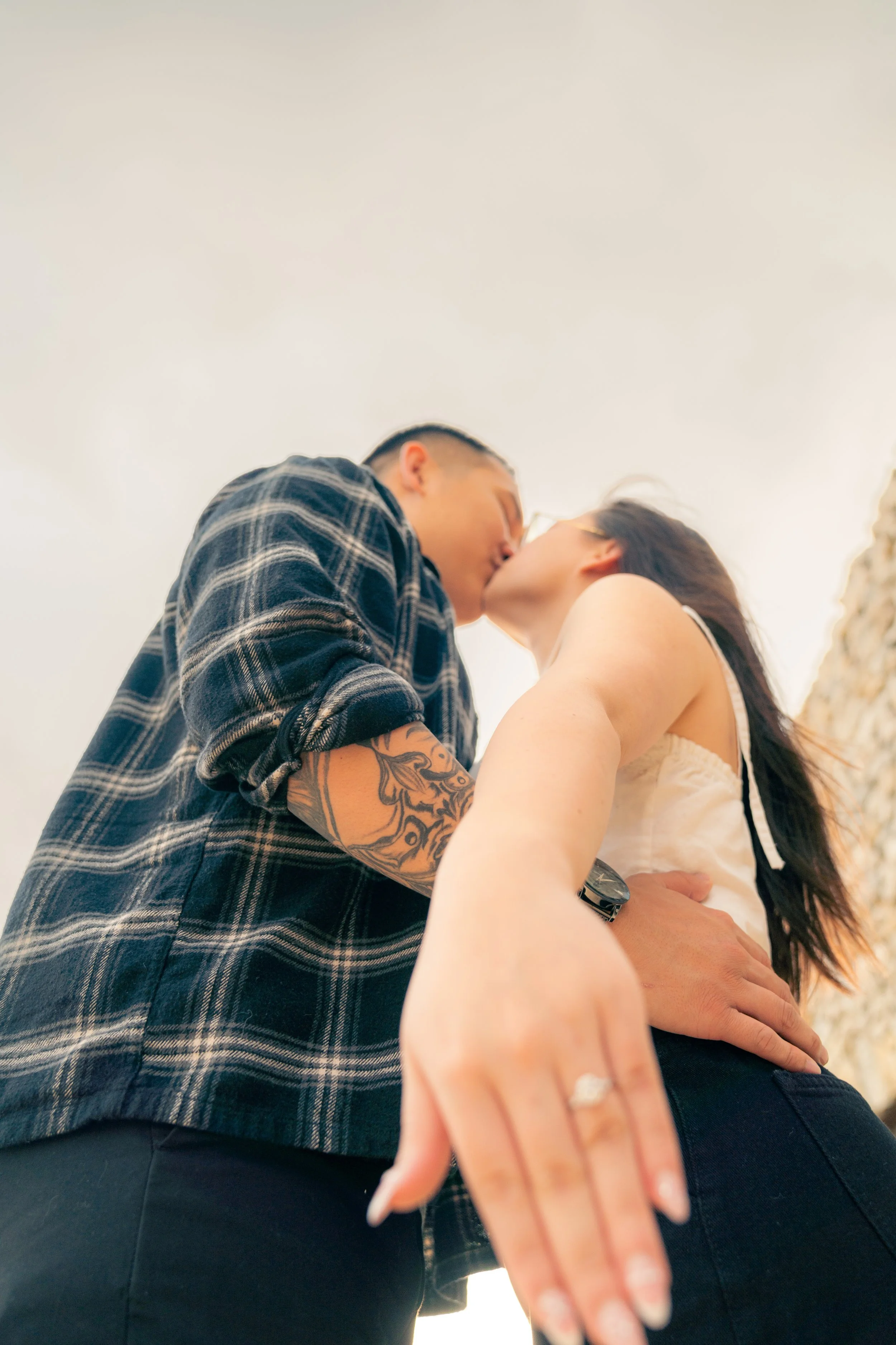 A couple kissing outdoors, with the photo taken from a low angle, showing their bodies and faces close together.