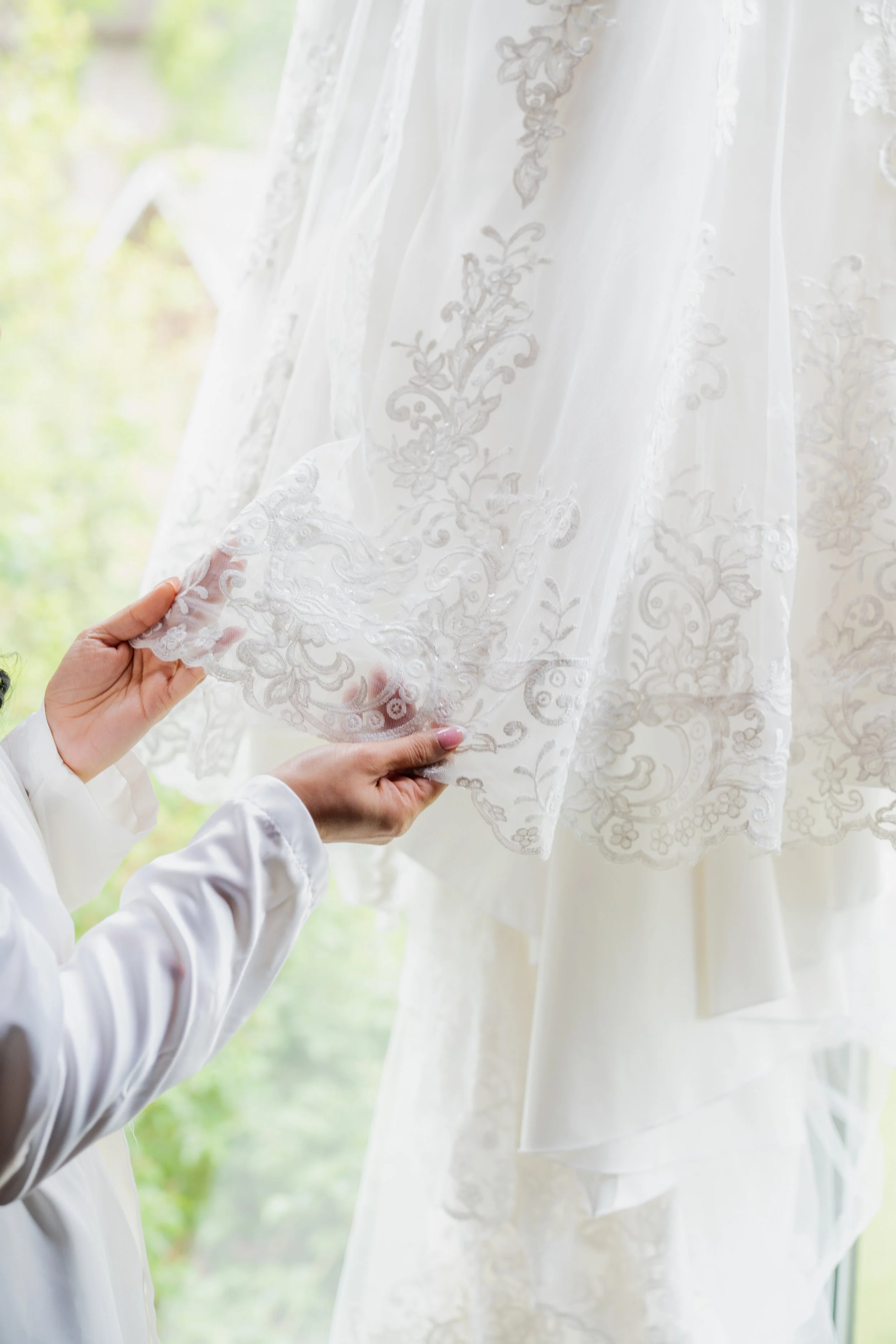 A person holding the corner of a sheer white curtain with floral embroidery, with another fabric visible behind it.