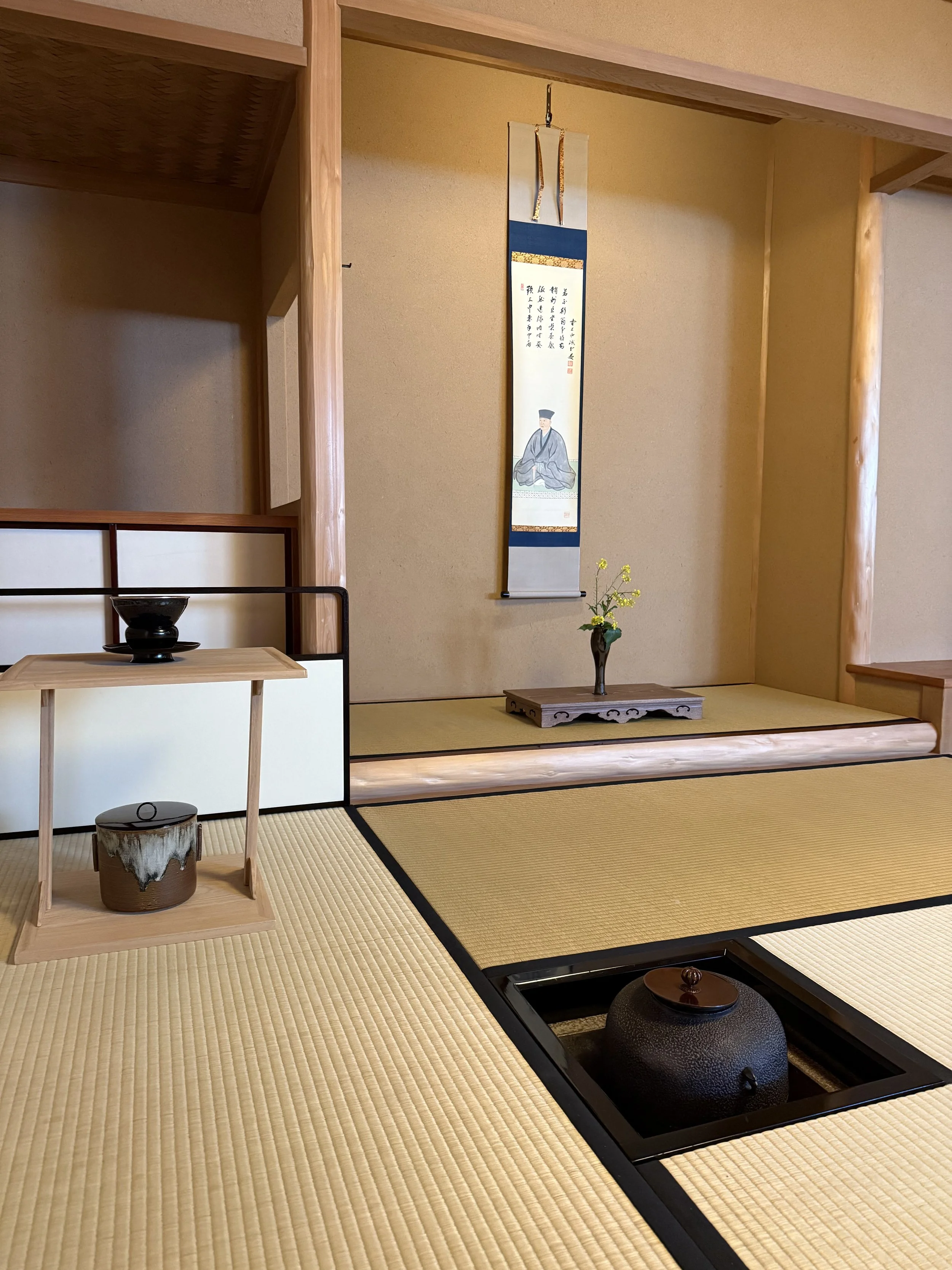 Traditional Japanese teaoom with a hanging scroll, a flower vase, and a tea kettle.