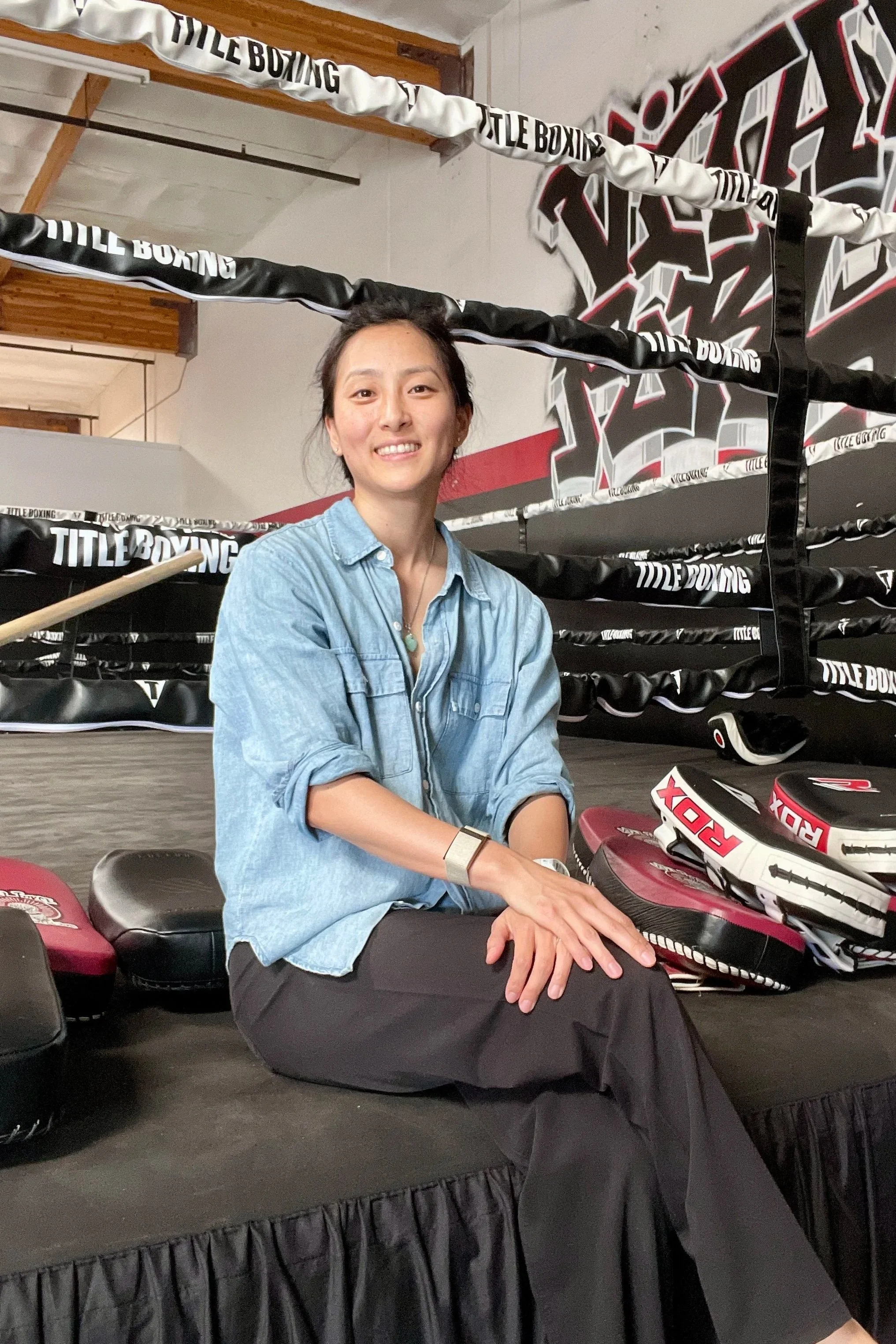 female sports physical therapist sitting with hand on lap legs crossed smiling while sitting on a boxing ring in a muay thai gym
