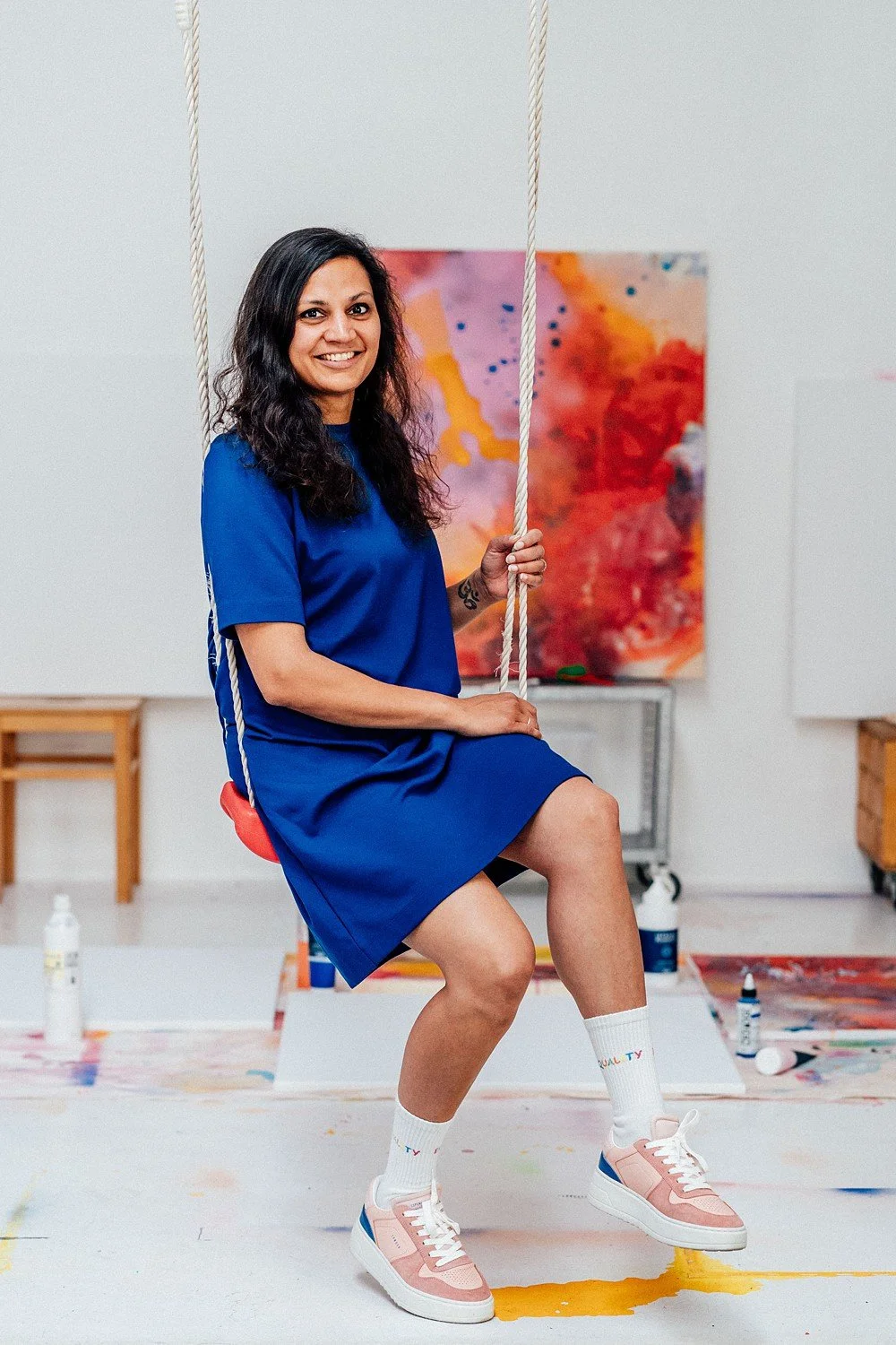 Frau in blauer Kleidung sitzt auf einer Schaukel mit Farbspritzern im Kunststudio.