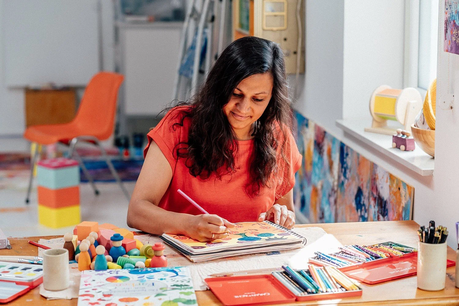 Eine Frau arbeitet in einem Kunststudio und malt auf einem Skizzenblock, umgeben von Farben und Malmaterialien.