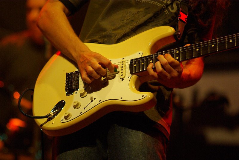 A person playing a yellow electric guitar with a white pickguard.