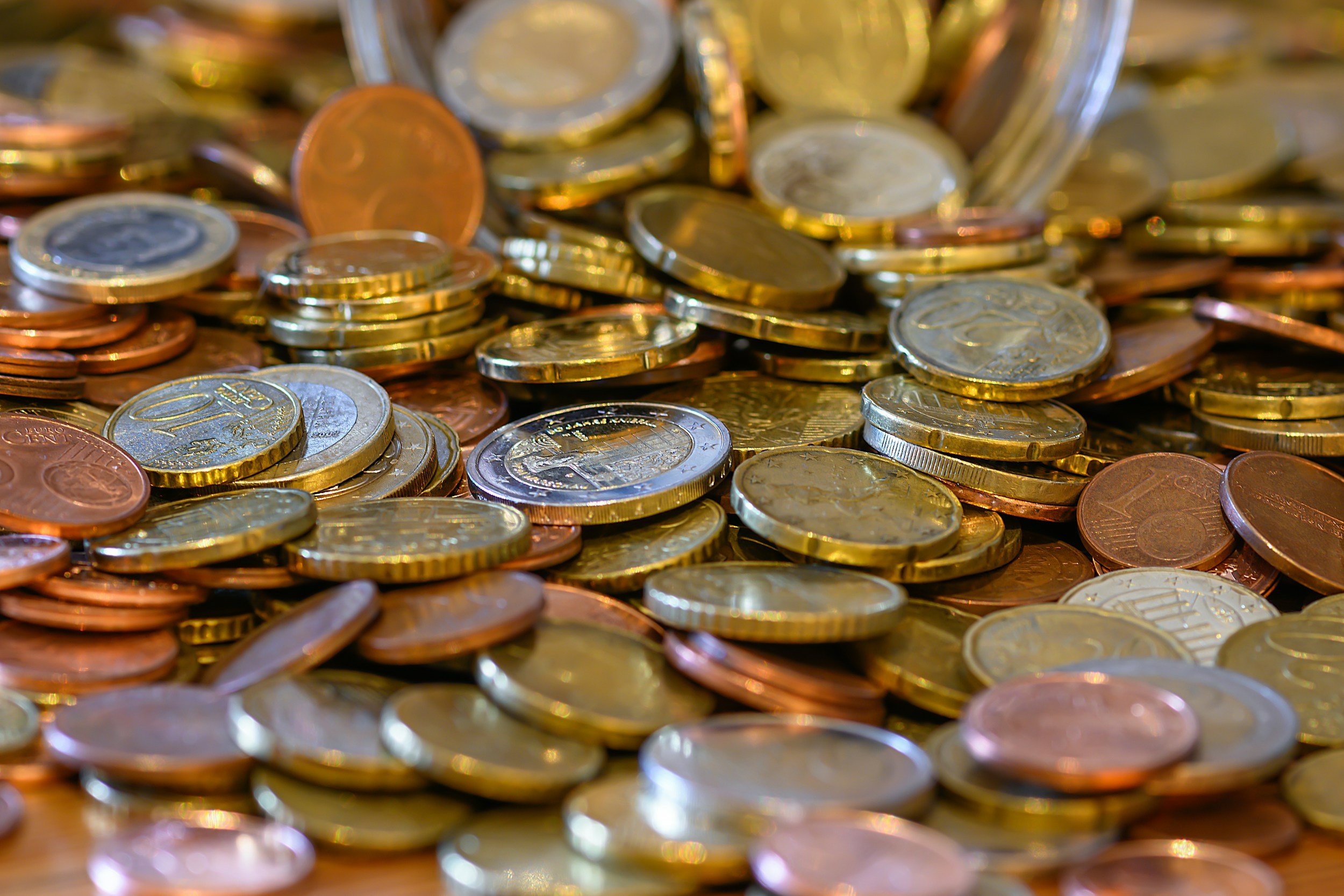 A close-up view of various euro coins, including copper-colored and gold-colored coins, scattered on a wooden surface.