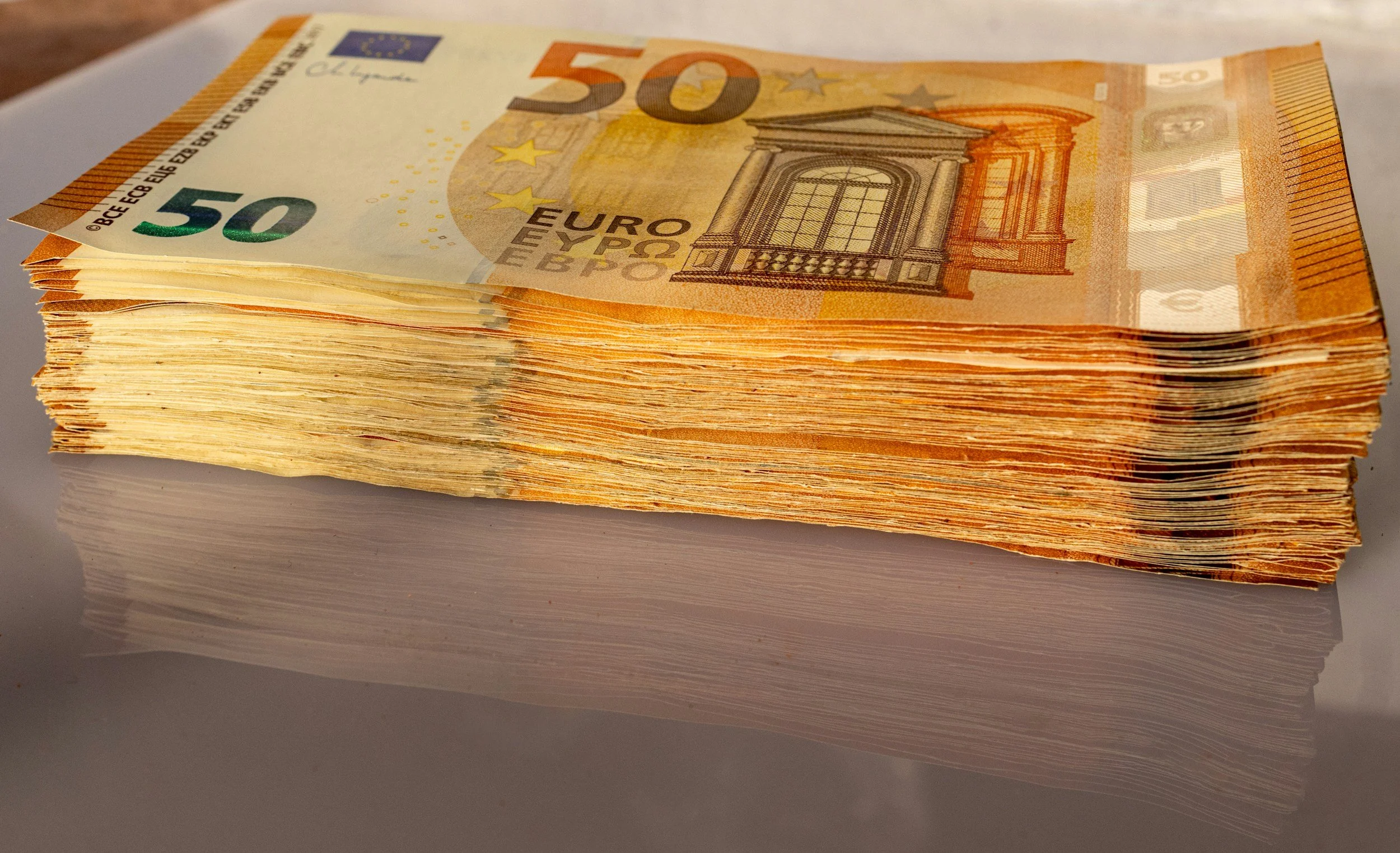Stack of 50 euro banknotes on a reflective surface.