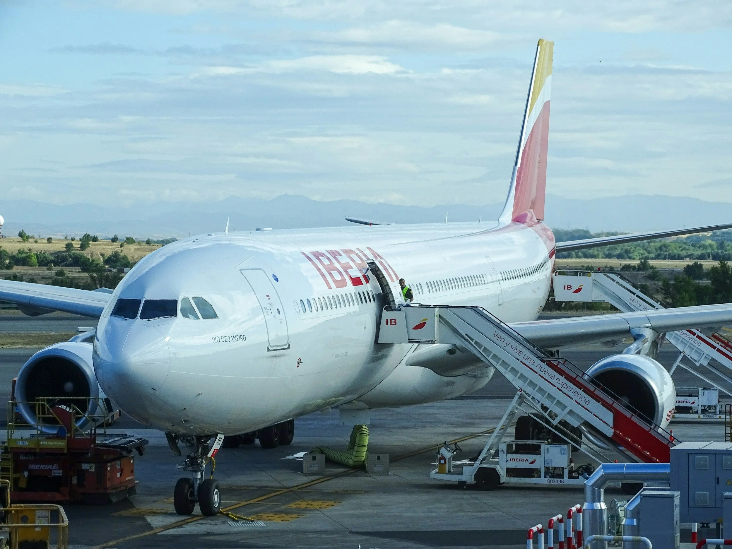 An Iberia airplane parked at the airport gate, with boarding stairs and ground support equipment nearby.