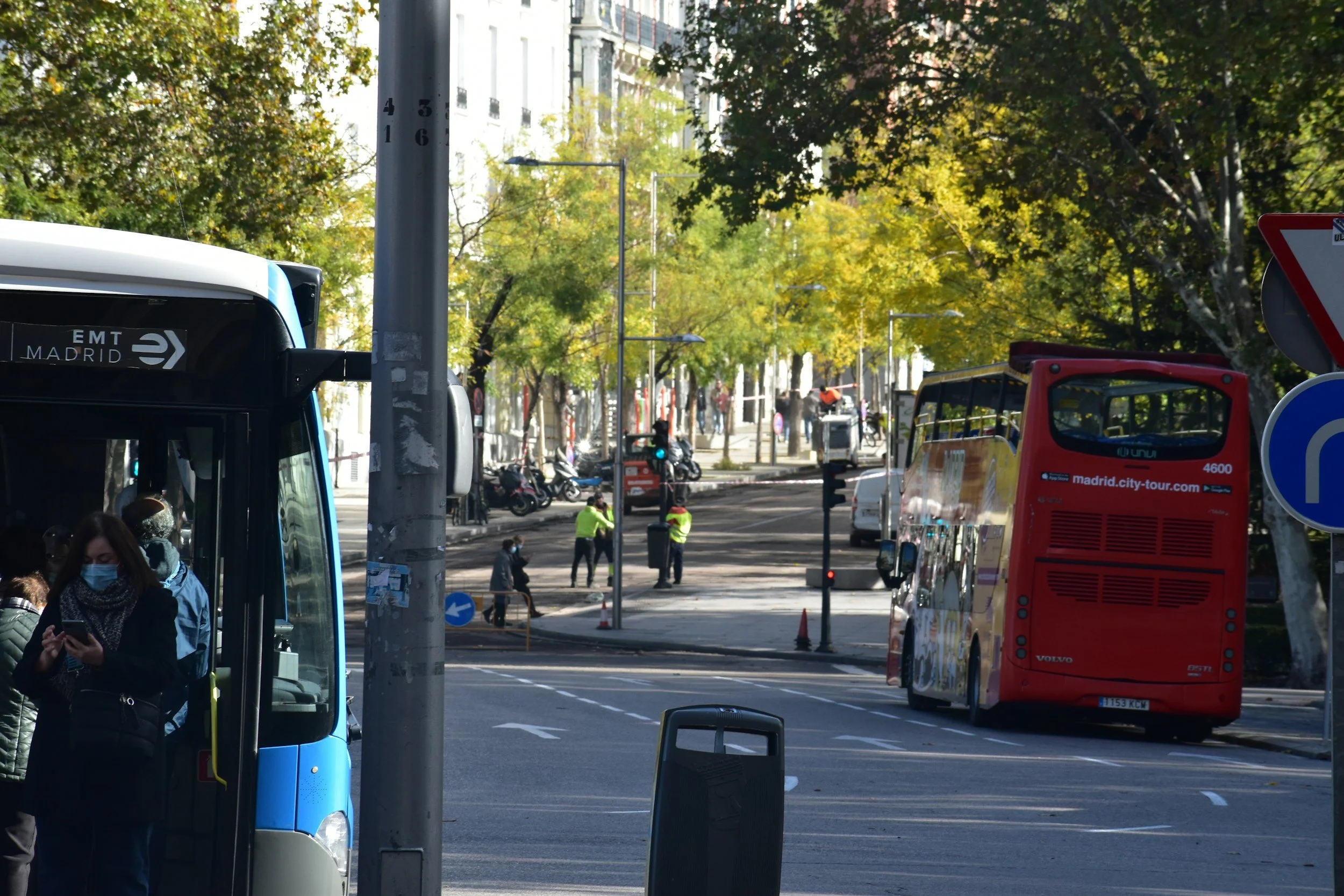 Street scene in Madrid with buses, pedestrians, and trees.