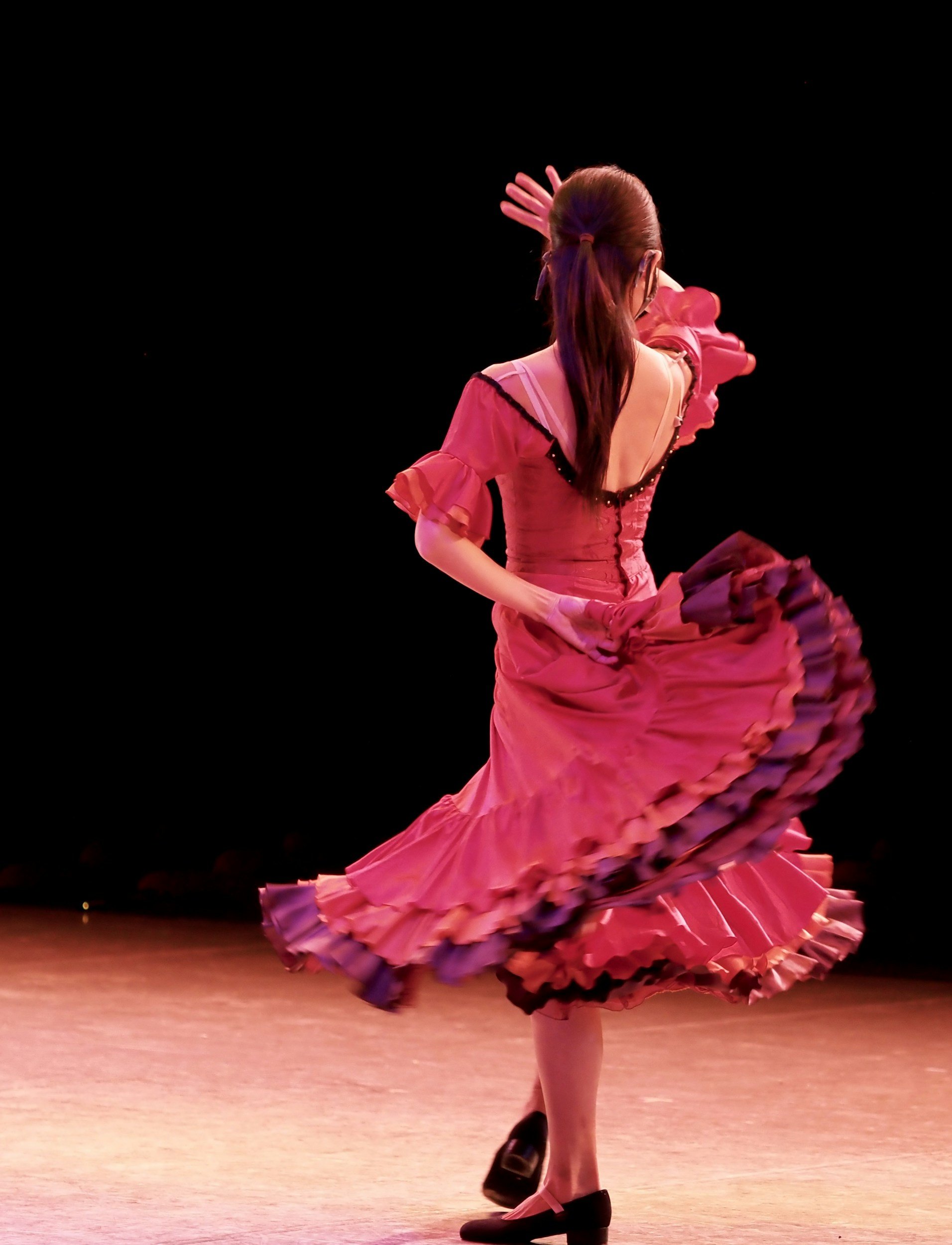 Dancer in a pink ruffled dress dancing on stage with a black background.