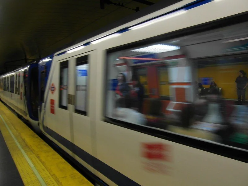 A subway train at a station with some passengers visible through the windows and people on the platform, illuminated by station lighting.