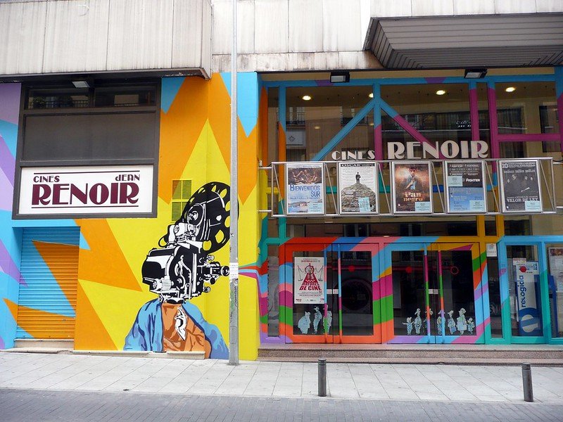 Colorful mural of a person with a vintage camera for a head outside Cines Renoir movie theater.