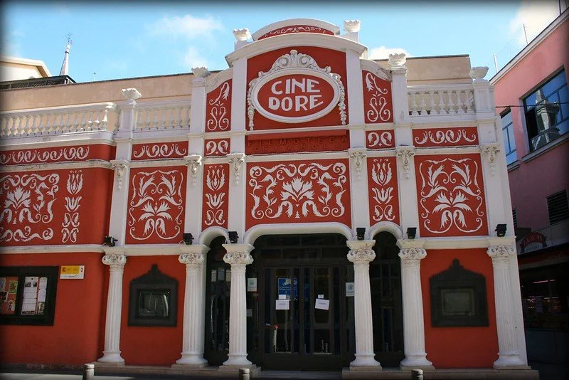 A building with ornate white and red architectural details, labeled 'CINE DORE,' resembling a vintage theater or cinema.