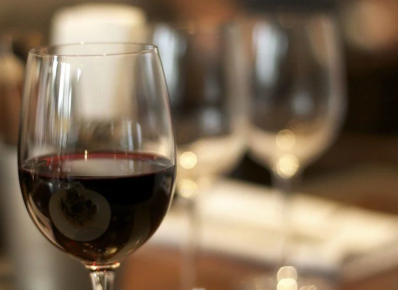 A glass of red wine in the foreground with two empty wine glasses in the background on a table.