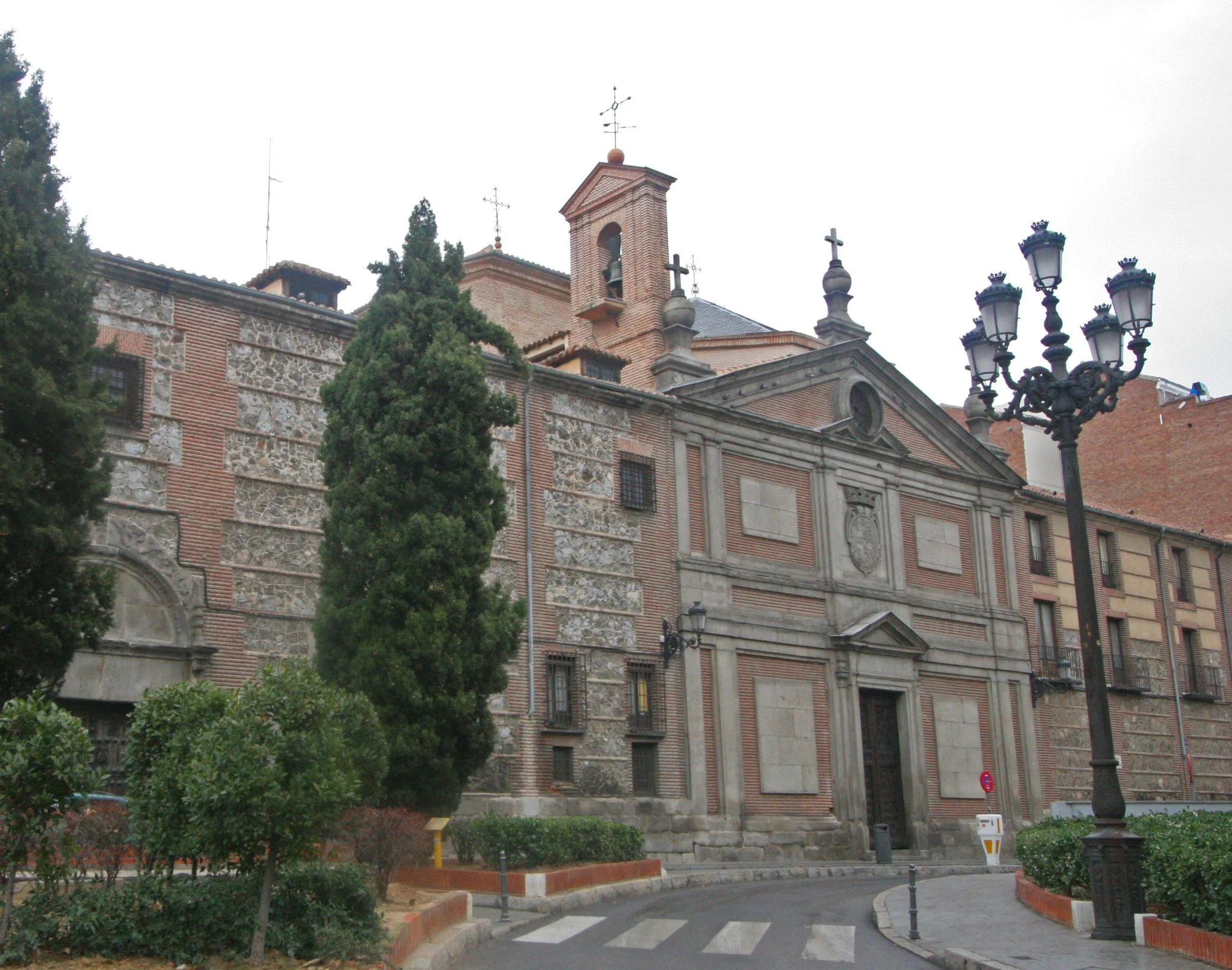 Historic church with stone and brick facade, ornate architectural details, tall trees, and a black vintage street lamp in foreground.