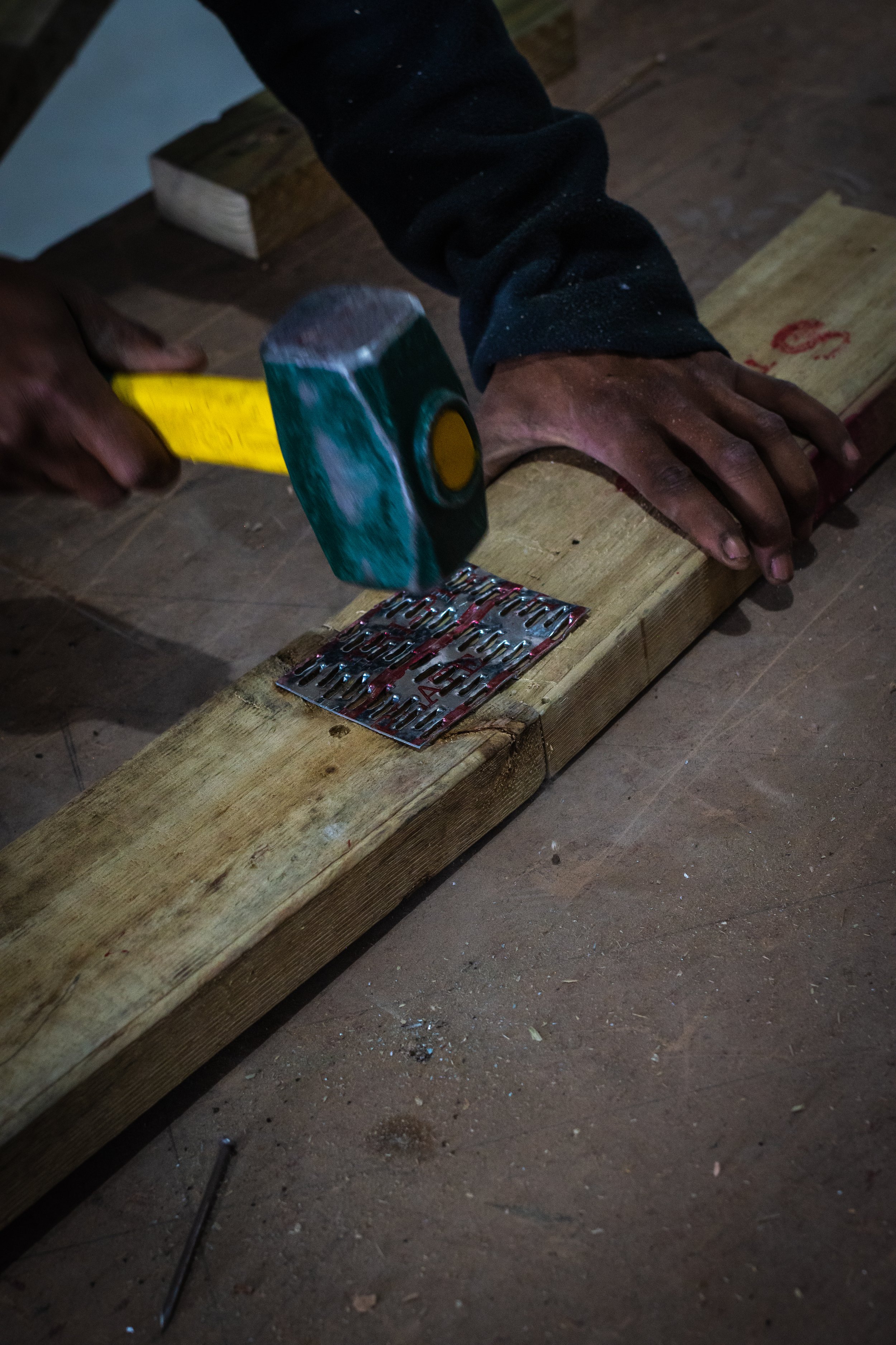 Person hammering a metal connector into wood on a workbench