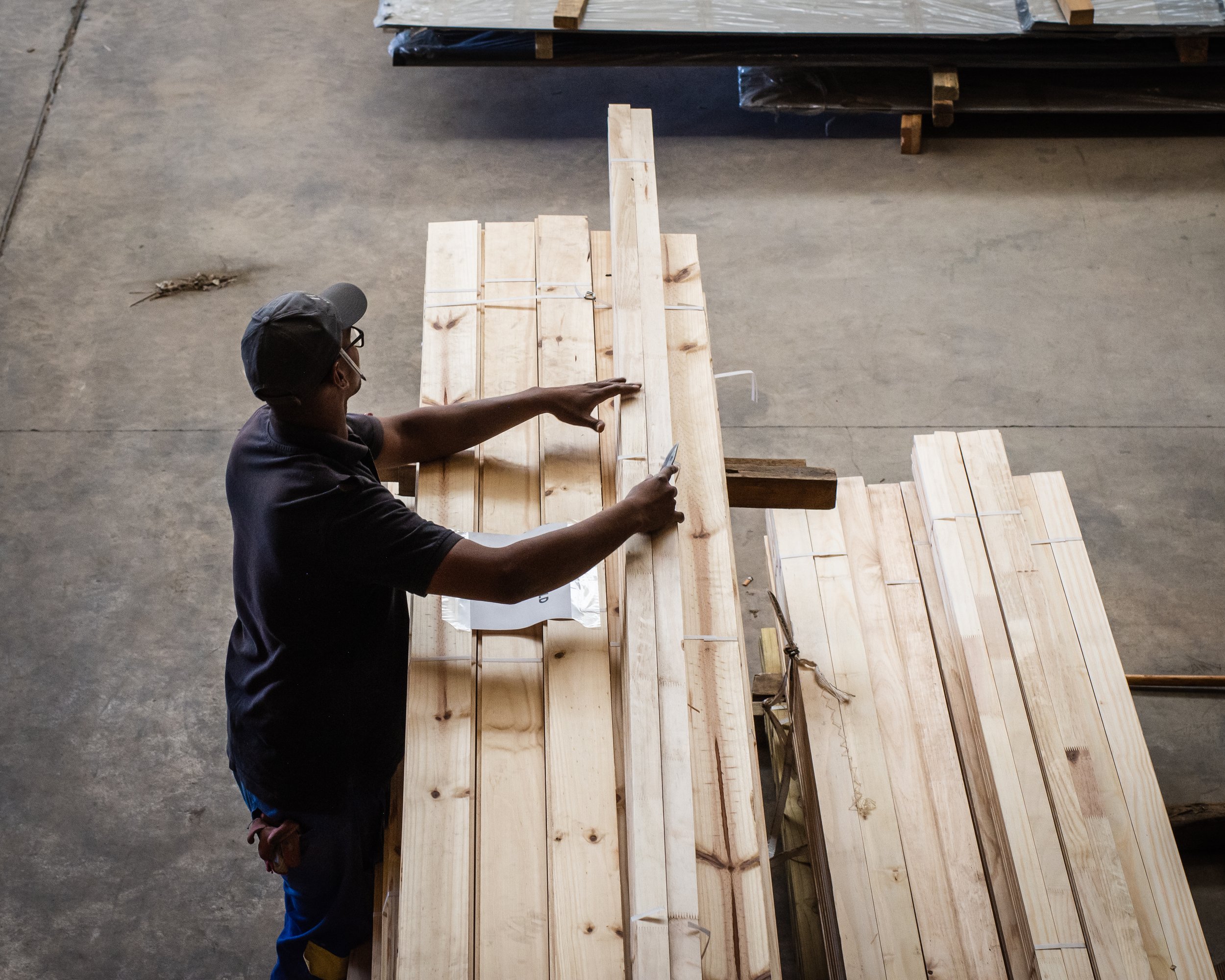 Person inspecting and measuring wooden planks on a warehouse floor.