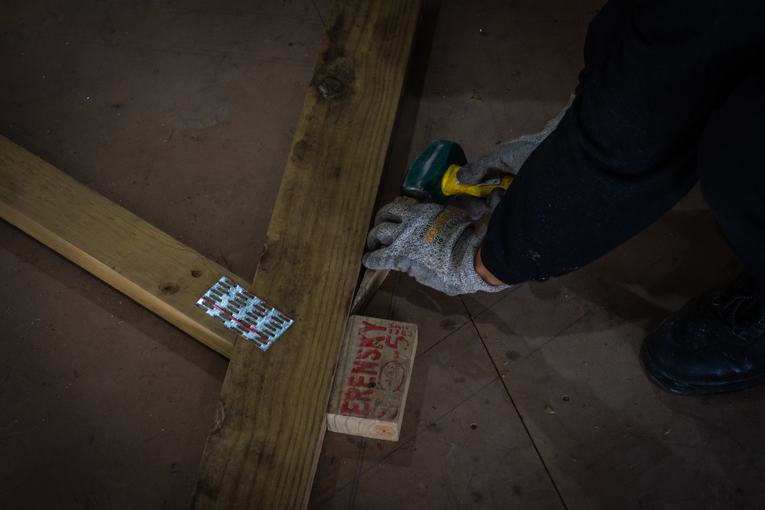 Person hammering wood with a mallet, wearing gloves