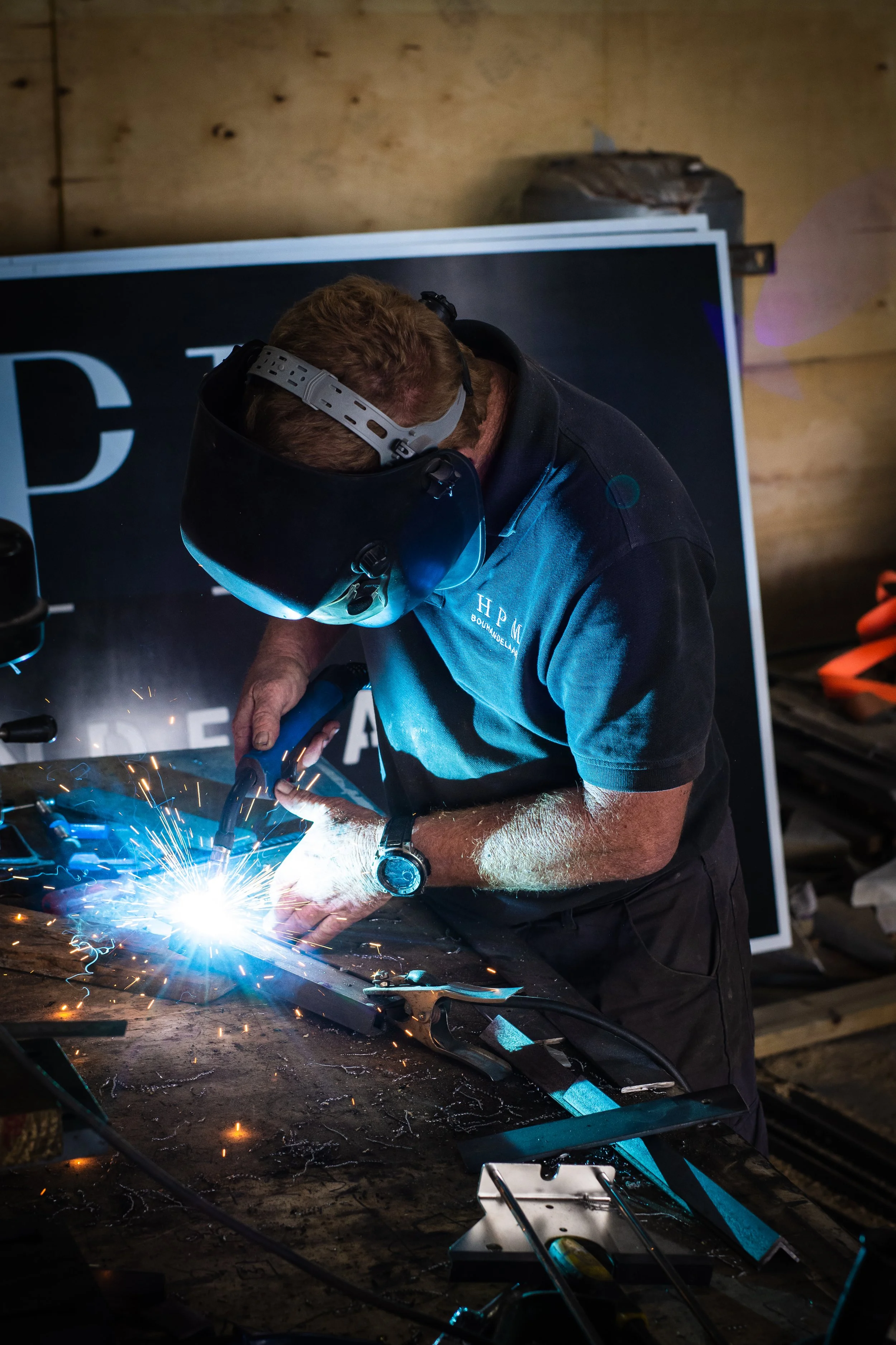 Person welding metal in a workshop, wearing protective gear and helmet, with sparks flying.