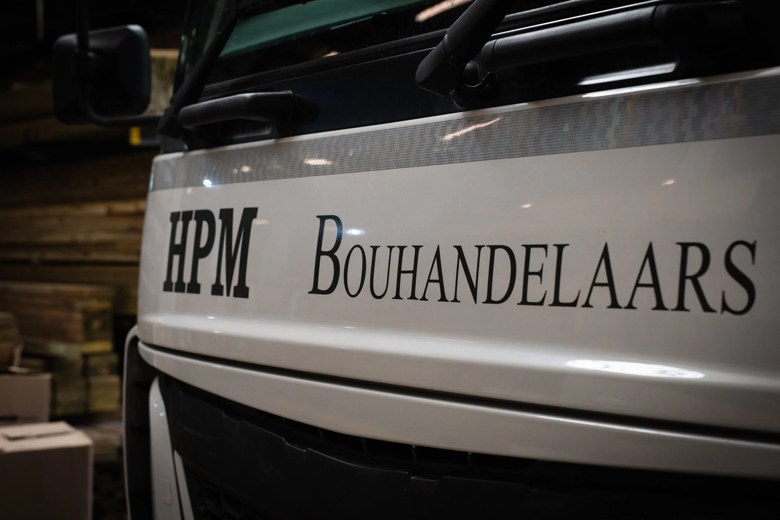 Close-up of a truck with "HPM Bouhandelaars" written on its side in a warehouse setting.