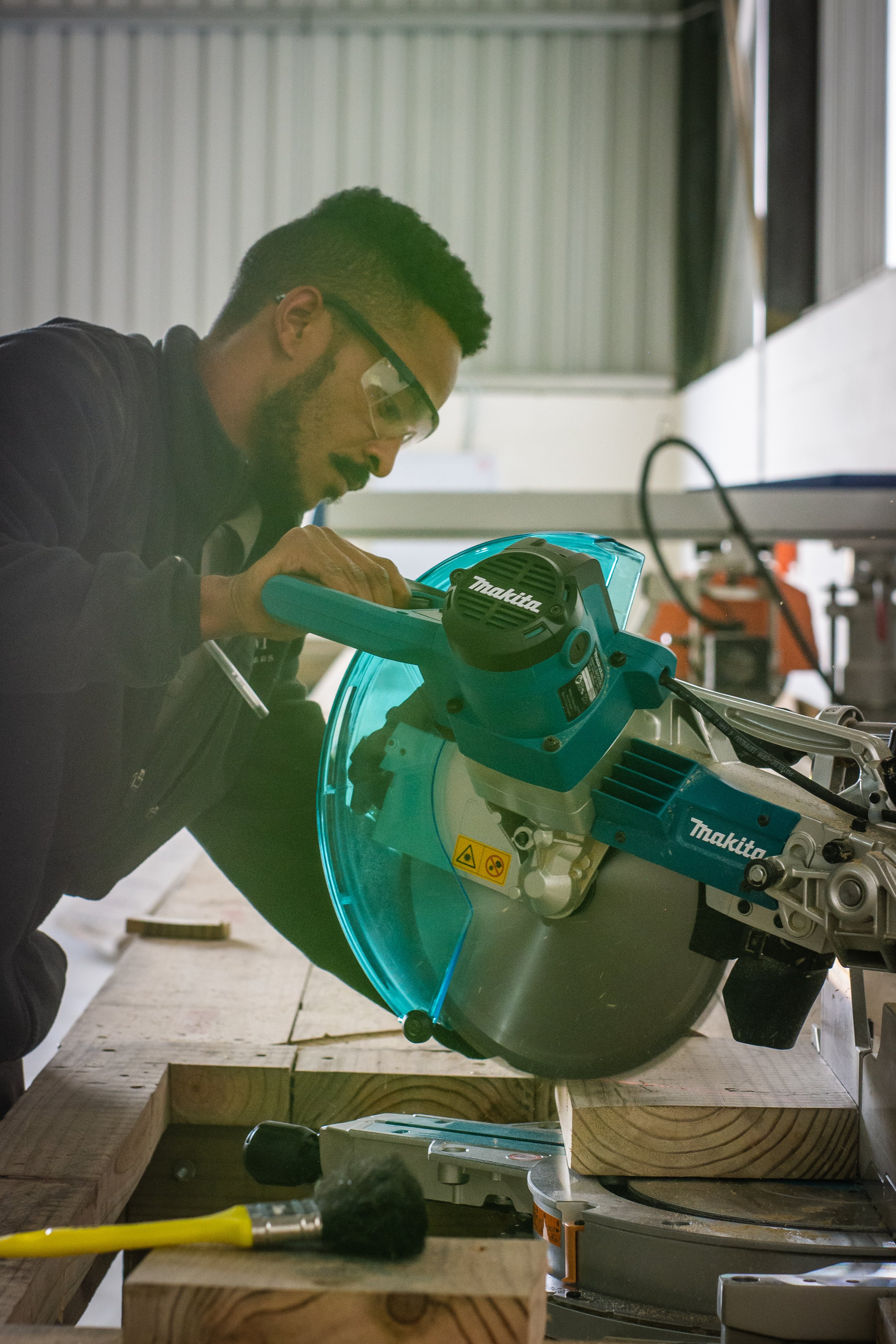 Person using a Makita miter saw to cut wood in a workshop