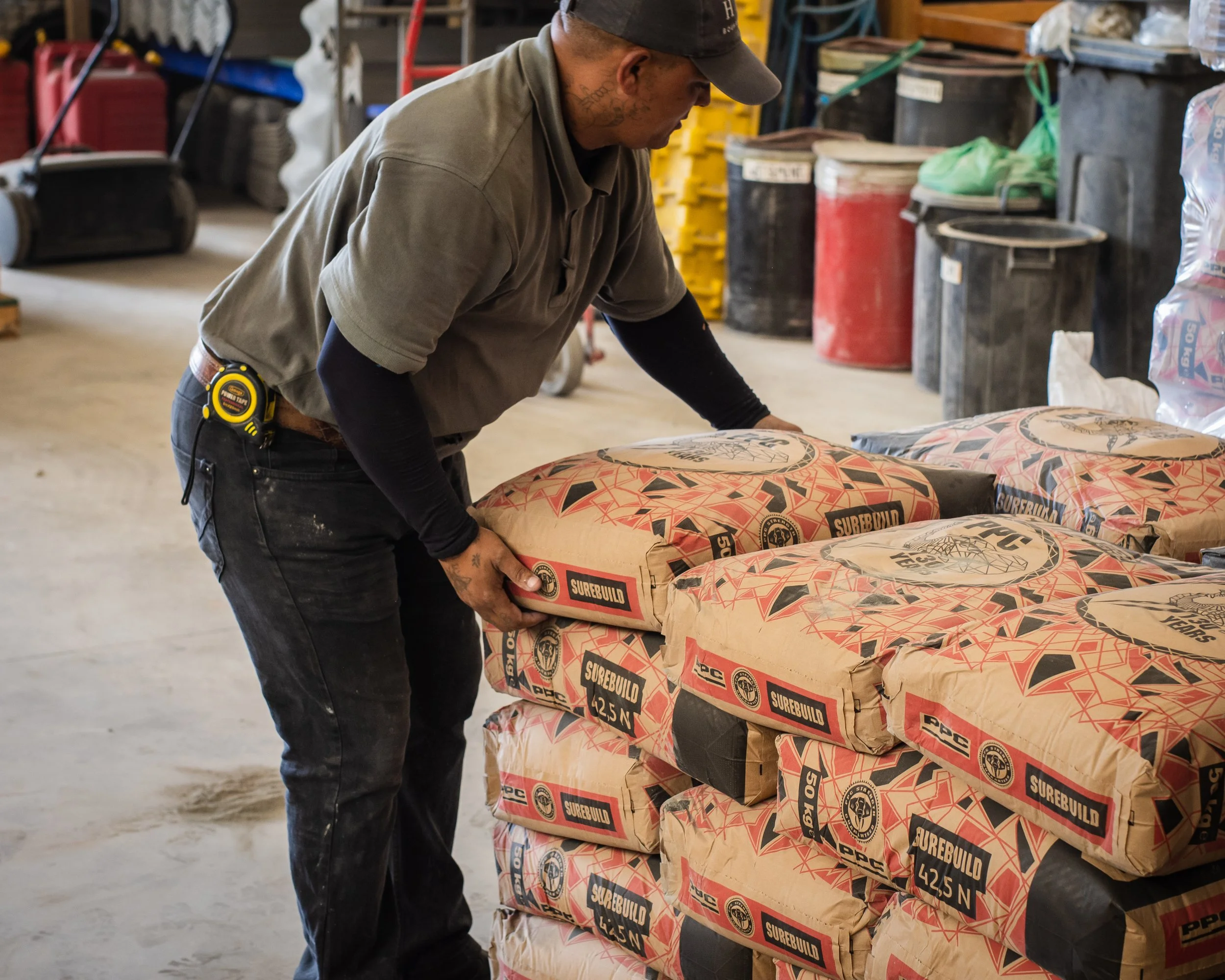 A person in a workshop stacking bags of Surebuild cement.
