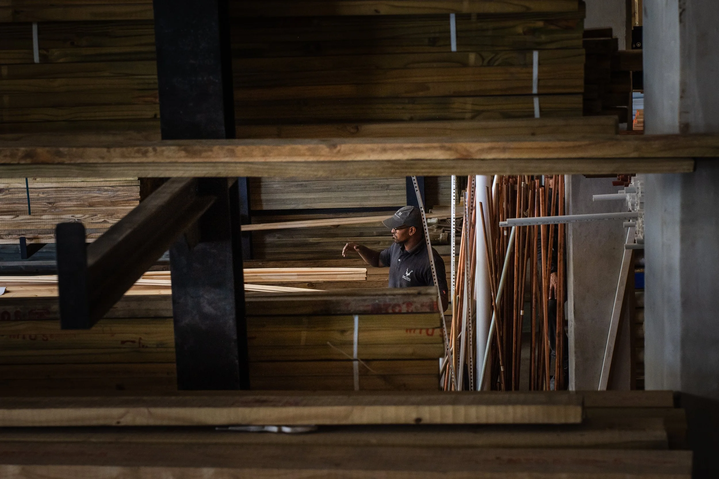Person organizing lumber in a wood storage area with stacked planks.