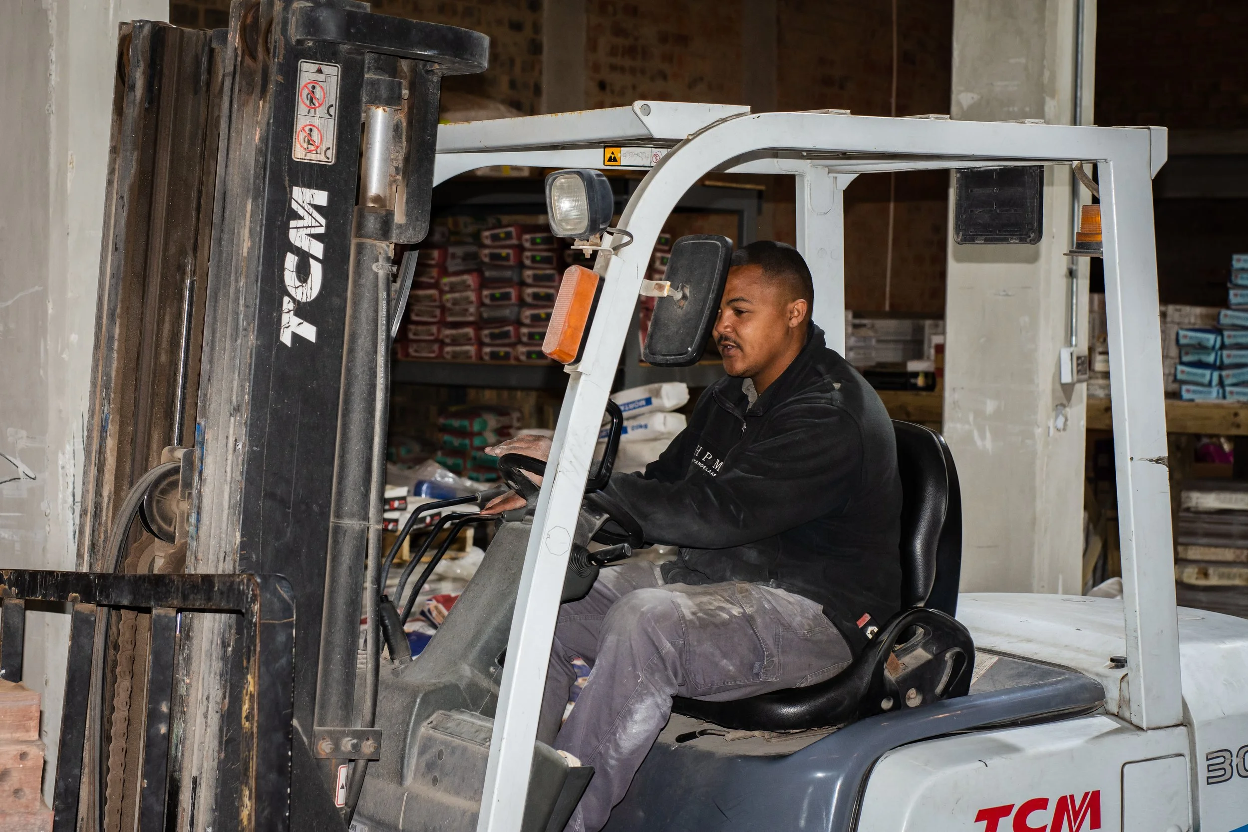 Man operating a forklift in a warehouse filled with stacked boxes and bags.