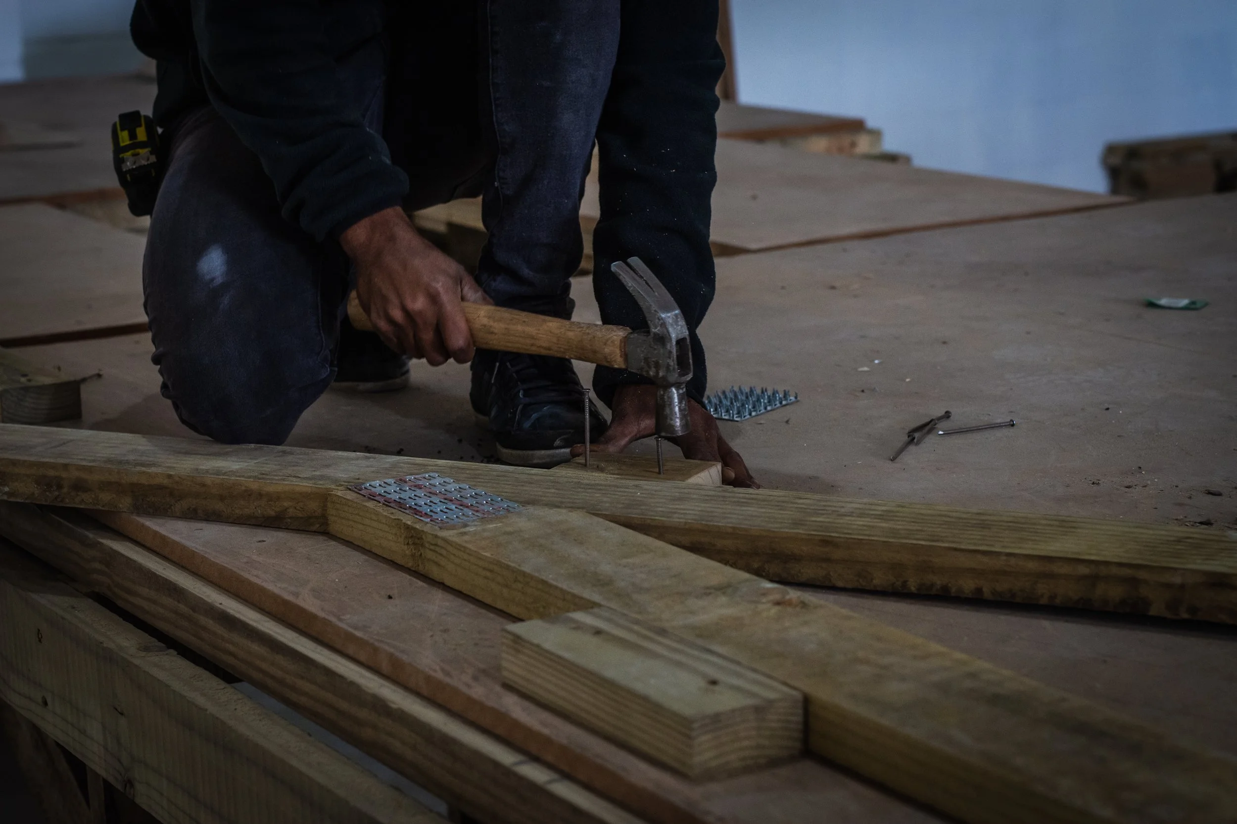Person using a hammer and nails on wooden beams during construction indoors.