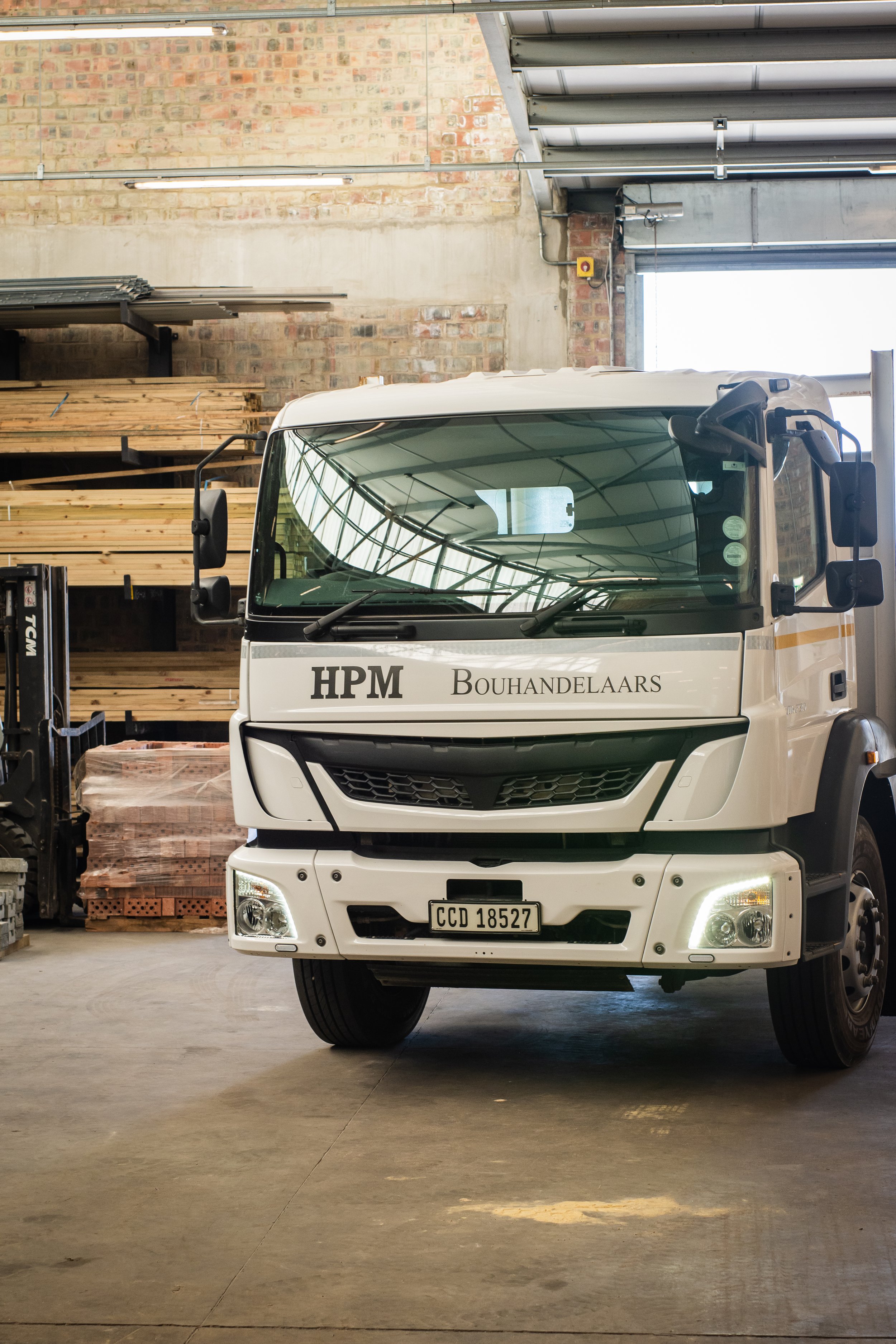 White delivery truck in warehouse with pallets and wood stacks