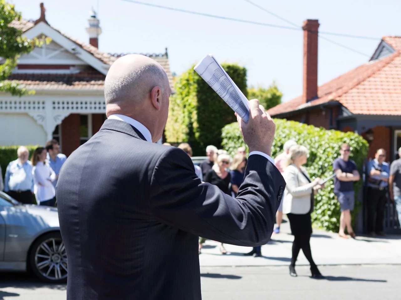 Home action on a sunny day, with an auctioneer in a suit holding paperwork in his hand and about to bring it down
