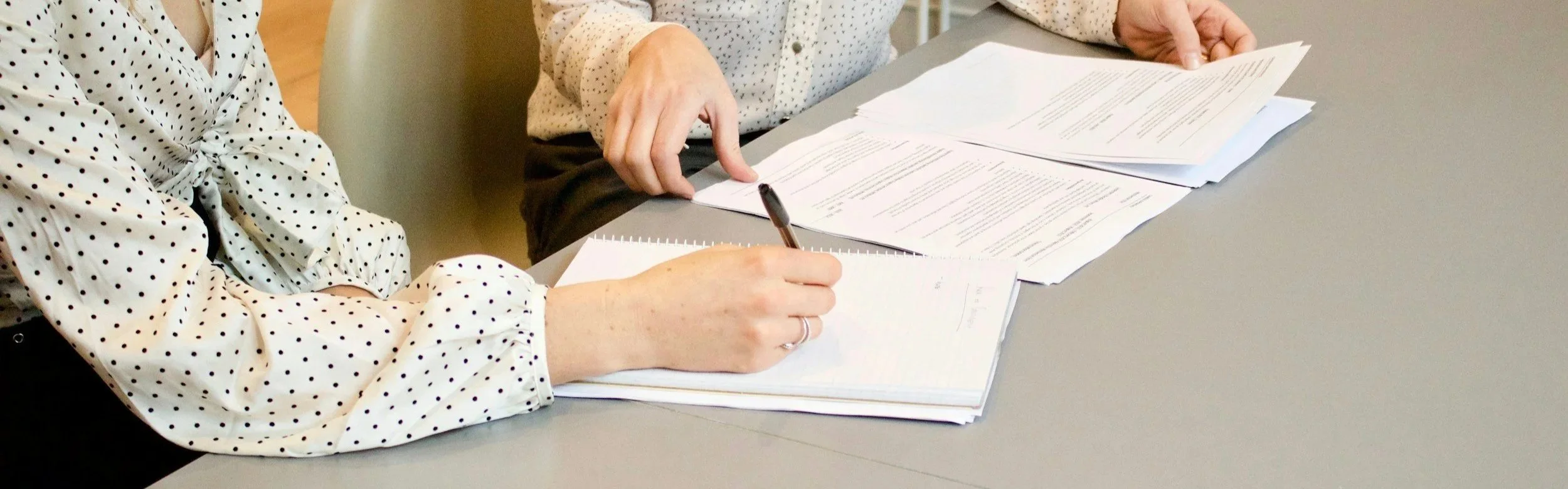Two people sitting at a table reviewing and taking notes on paperwork.
