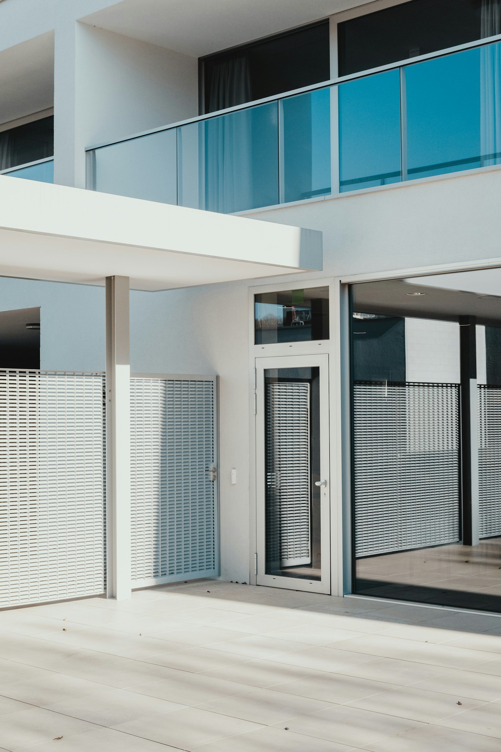 Modern apartment balcony with large sliding glass doors and a metal railing, featuring a white exterior wall and tiled floor