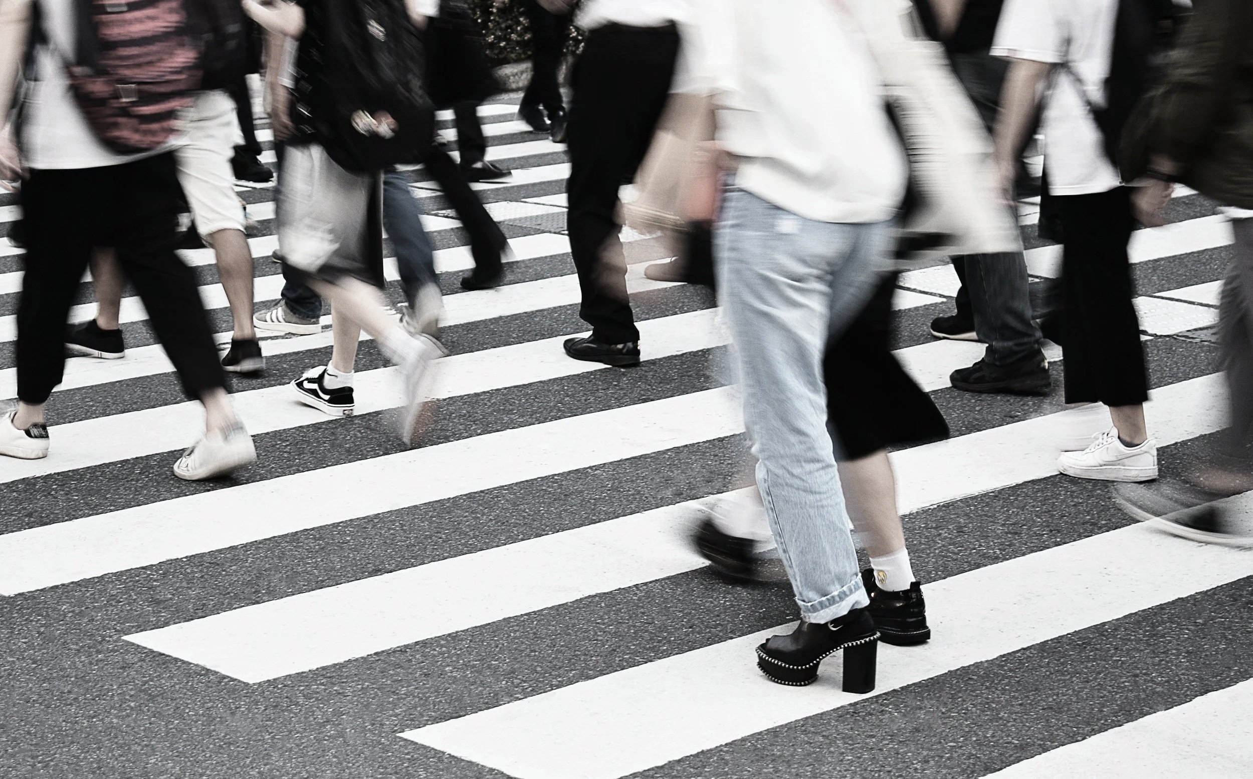 People walking across a black and white striped crosswalk on the street.