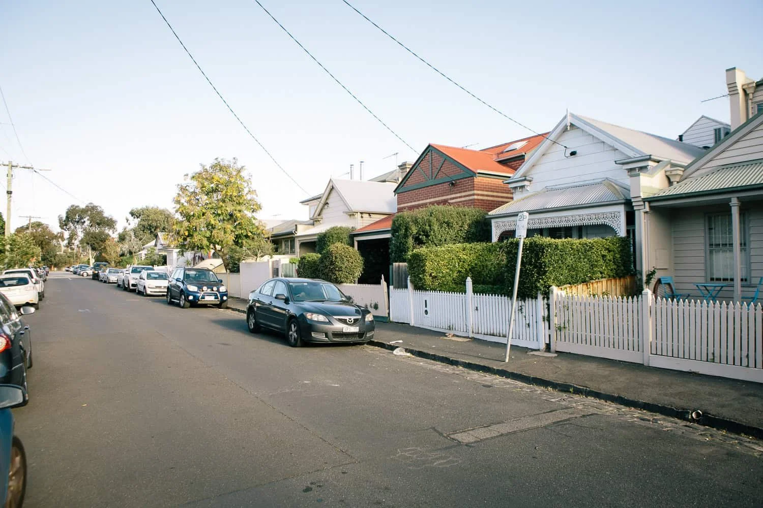 A residential street in St Kilda East, Melbourne, with parked cars along the curb, single-story houses with front yards and picket fences.