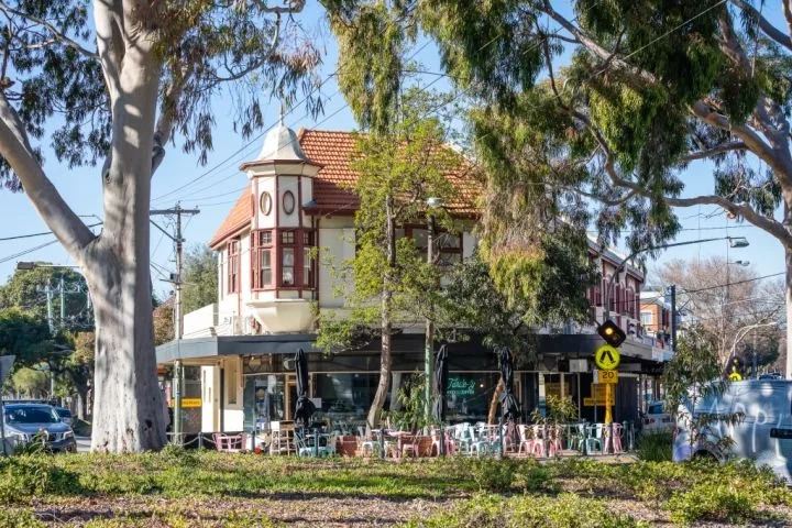 Ormond Road Elwood, Melbourne. A two-story building with a Victorian-style design, featuring a red-tiled roof, located on a street with outdoor seating and trees in front.