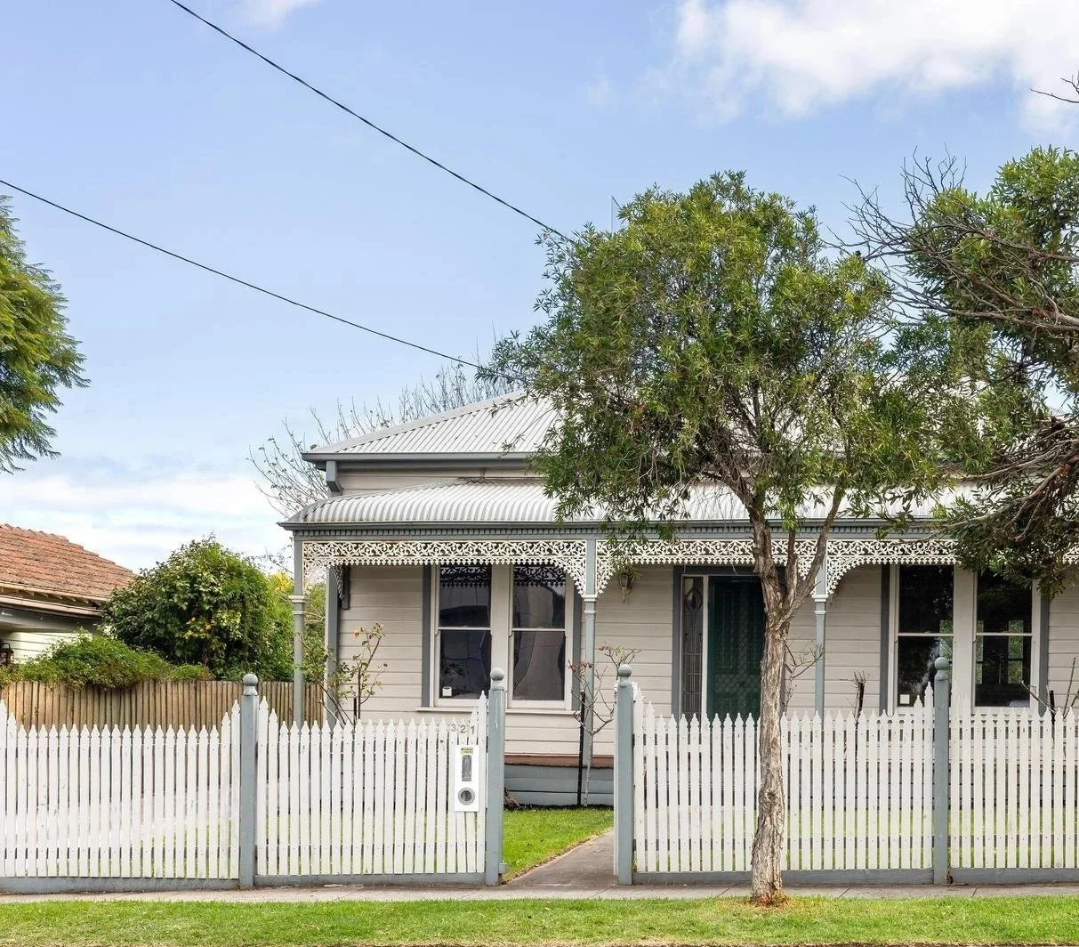 A vintage-style house in Ormond, Melbourne with a white picket fence, two trees in front, and a clear sky in the background.