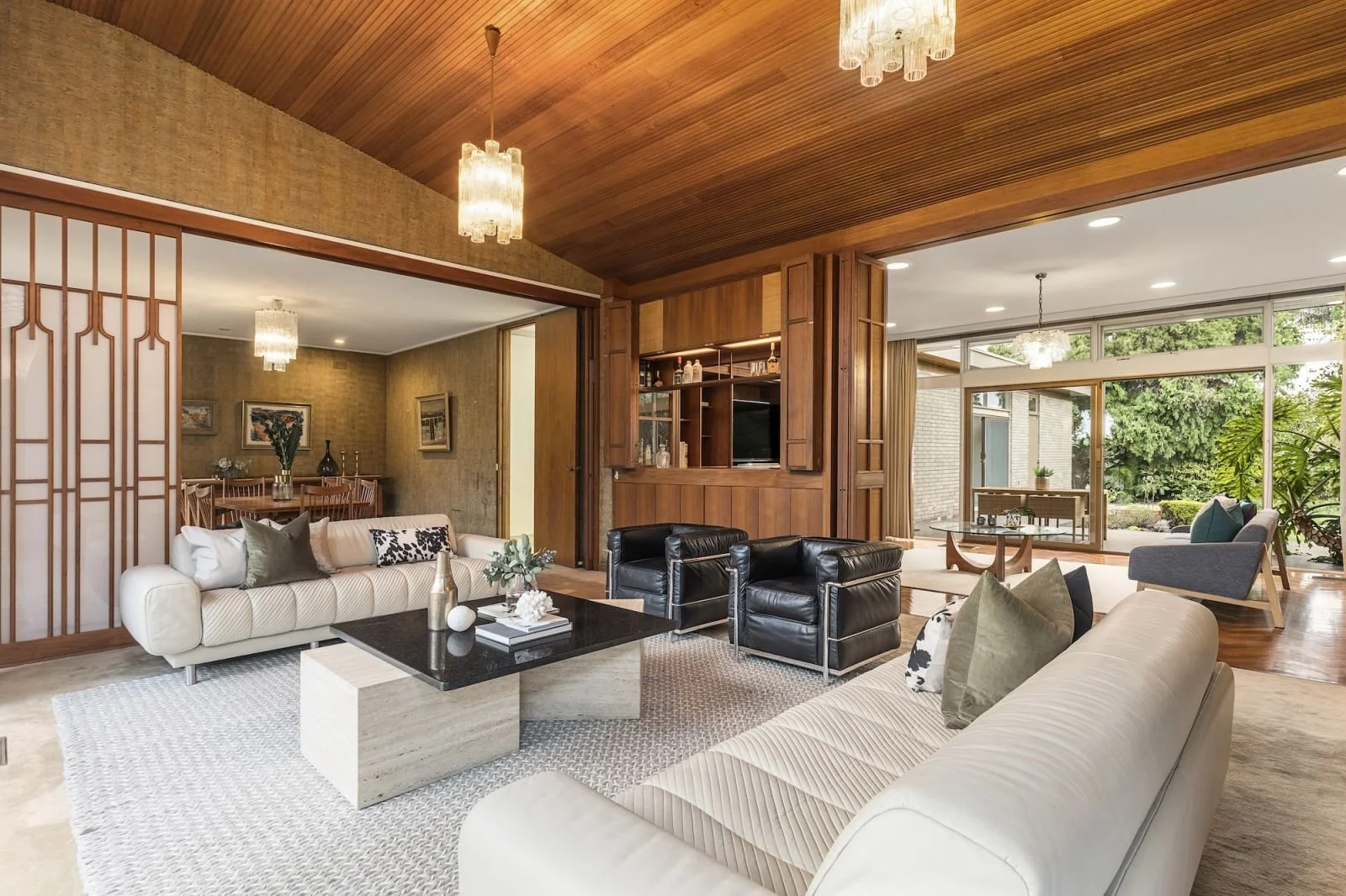 A spacious Mid Century Modern living room in Caulfield South with modern and mid-century furniture, including white and black sofas, a coffee table, and large windows.